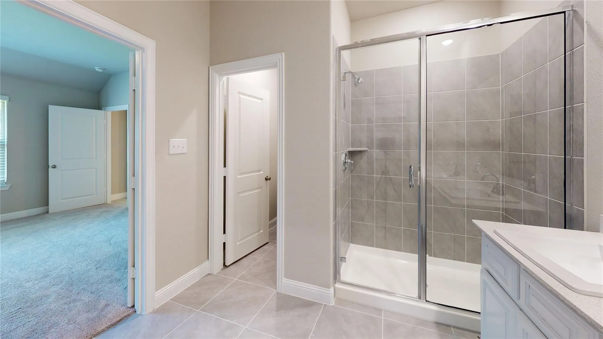 Glass-enclosed shower with gray tiled walls, white shower base, and a built-in shower shelf