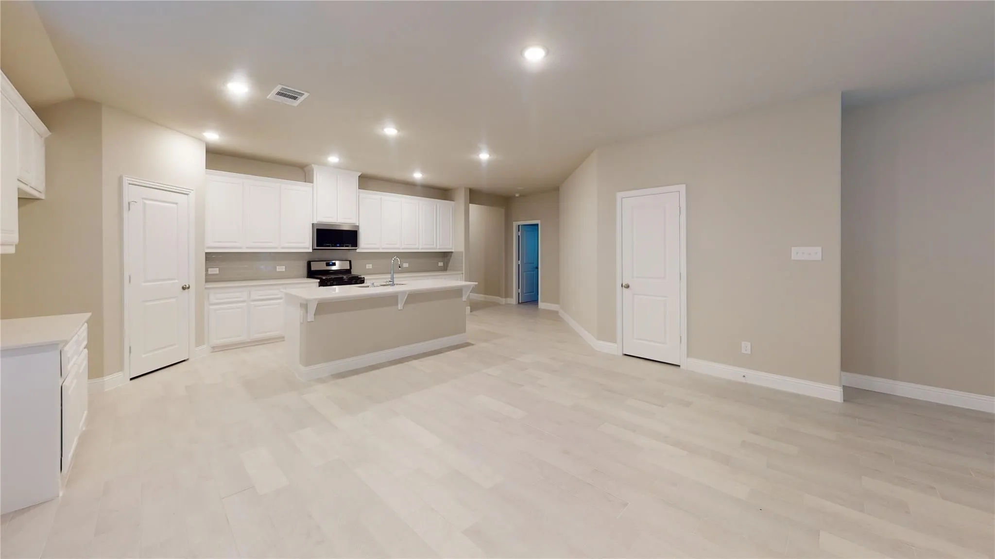 Spacious kitchen with a central island, recessed lighting, white cabinetry, a stainless steel microwave, and wood-finish flooring
