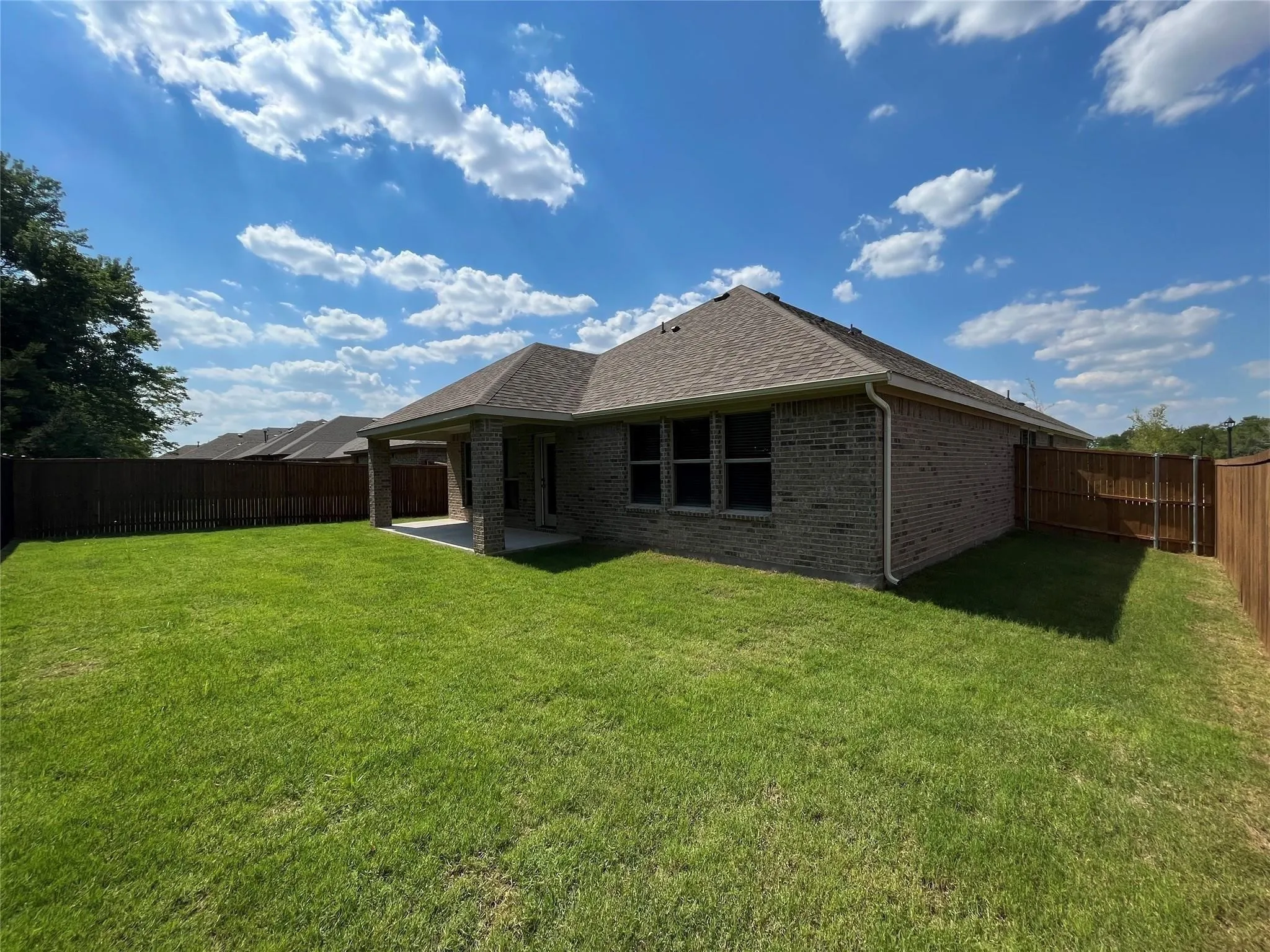 Expansive backyard featuring a manicured lawn, full privacy fencing, and a covered patio area