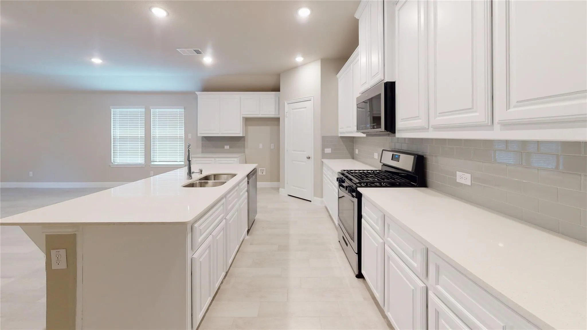 White kitchen cabinetry with stainless steel appliances, light countertops, subway tile backsplash, and a central island featuring a double-basin sink