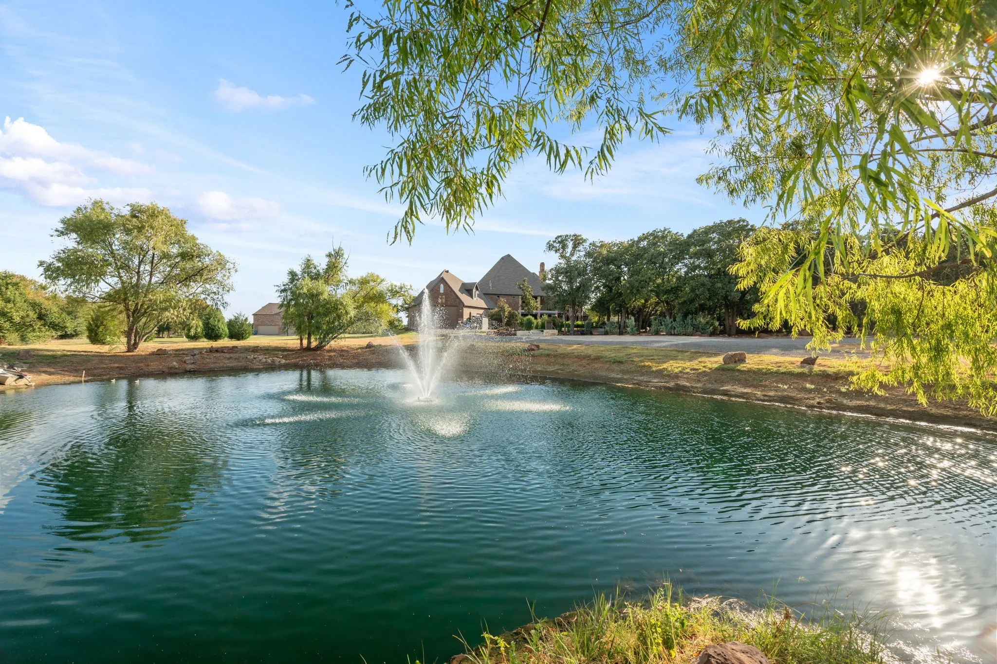 Expansive pond with a central fountain, stocked with fish and surrounded by mature trees and natural landscaping