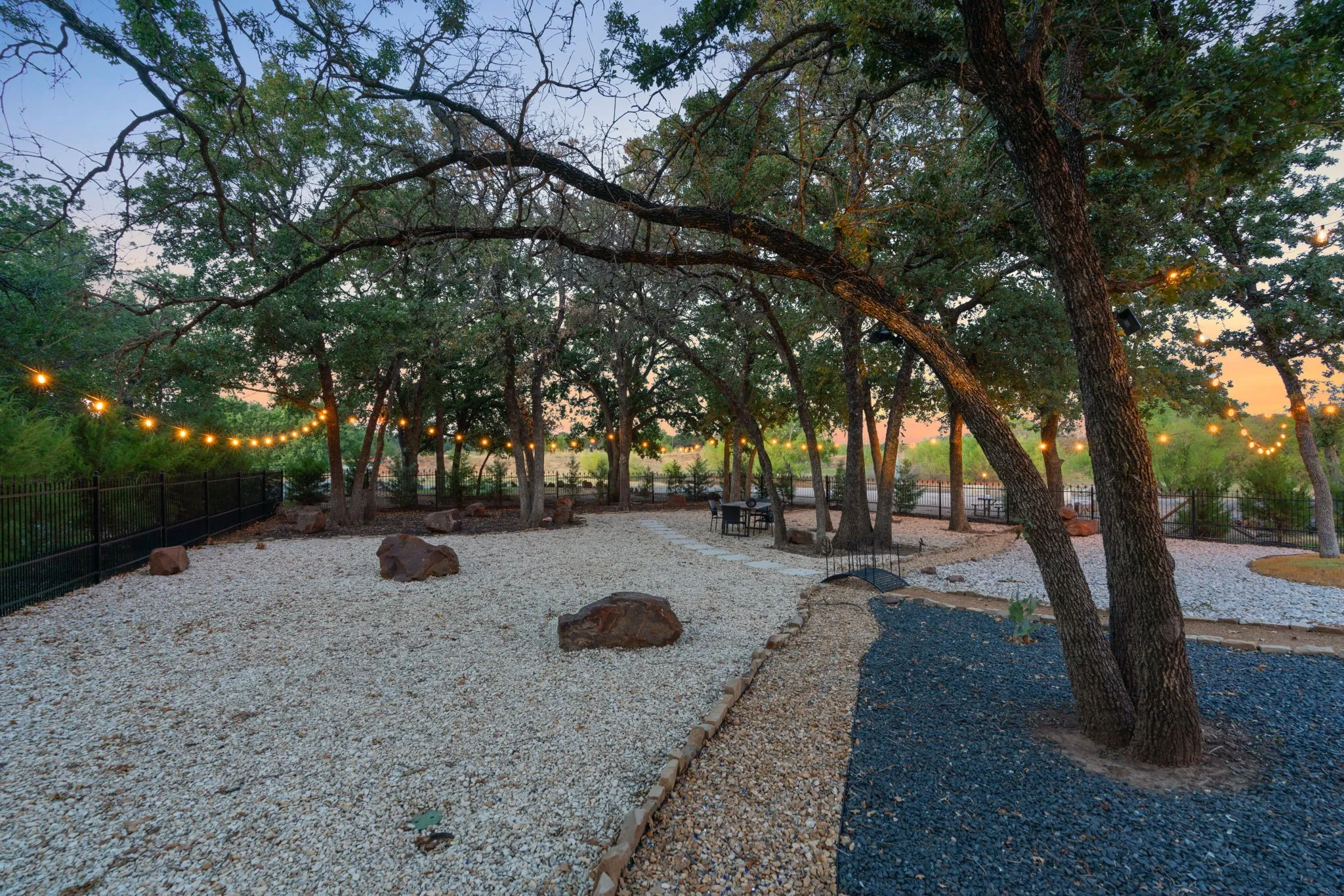 Landscaped outdoor area featuring multiple mature trees, string lighting, and diverse ground cover