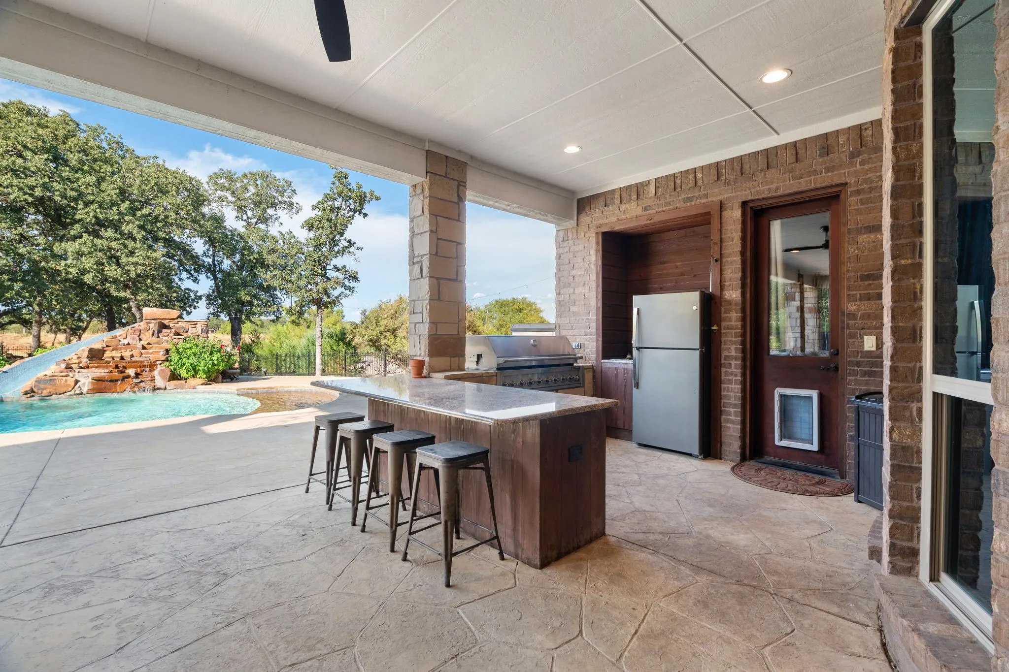 Covered patio with a built-in outdoor kitchen, ceiling fan, and recessed lighting and living area with stone fireplace and wired for TV
