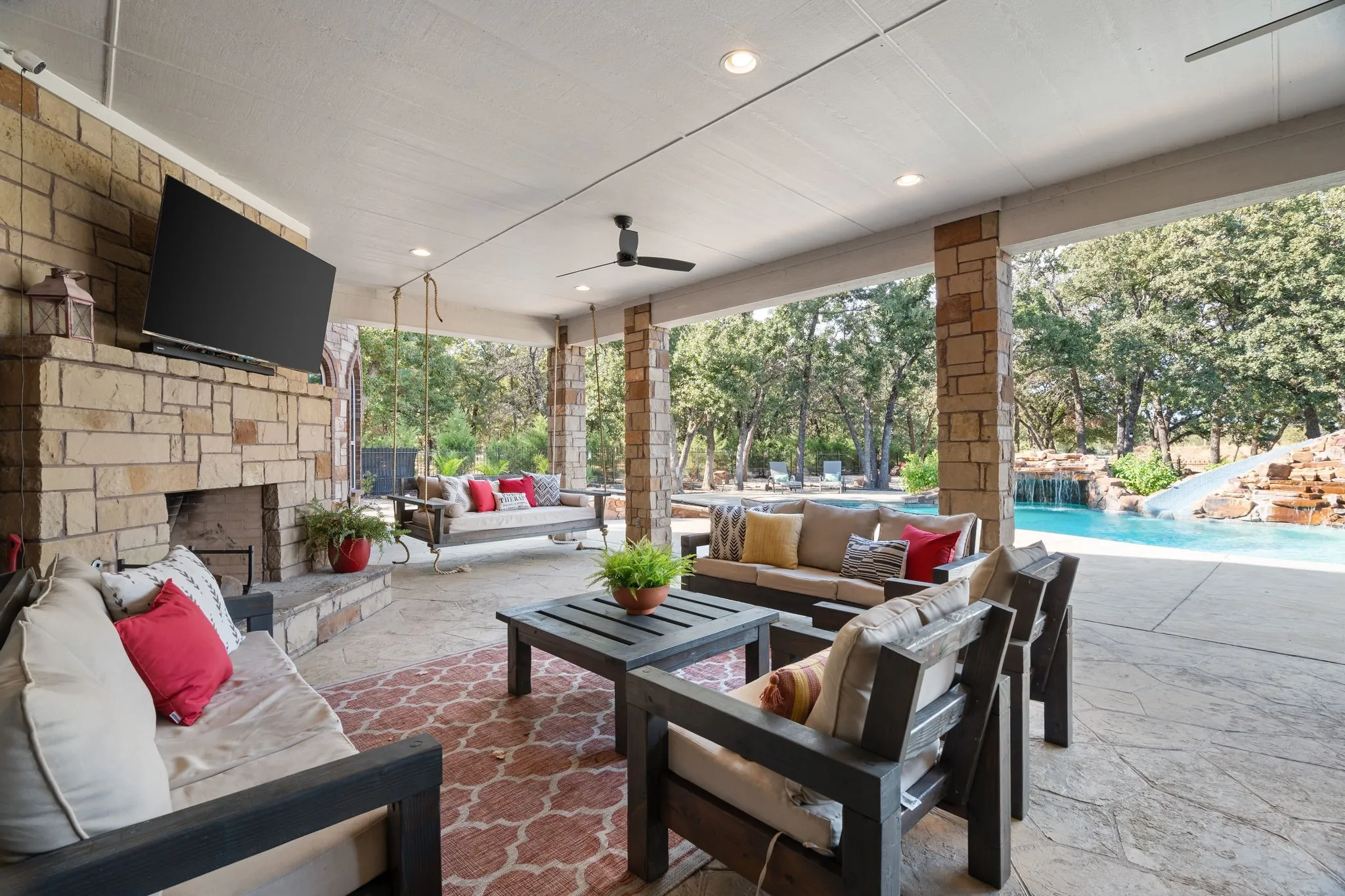 Covered outdoor patio featuring a stone fireplace wired for TV, recessed lighting, and a ceiling fan and outdoor kitchen