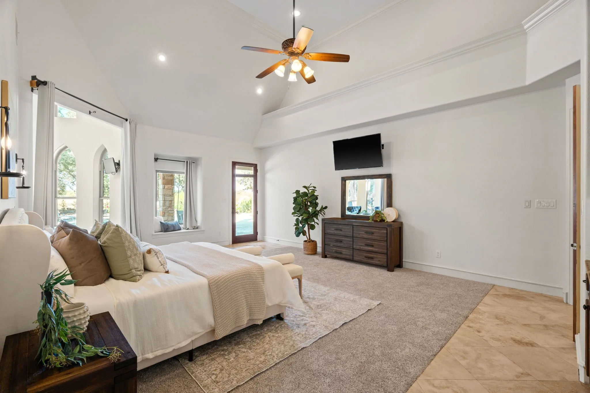 Vaulted ceiling with crown molding, recessed lighting, ceiling fan, and multiple windows including arched designs, wet bar, sitting area and exterior access to patio