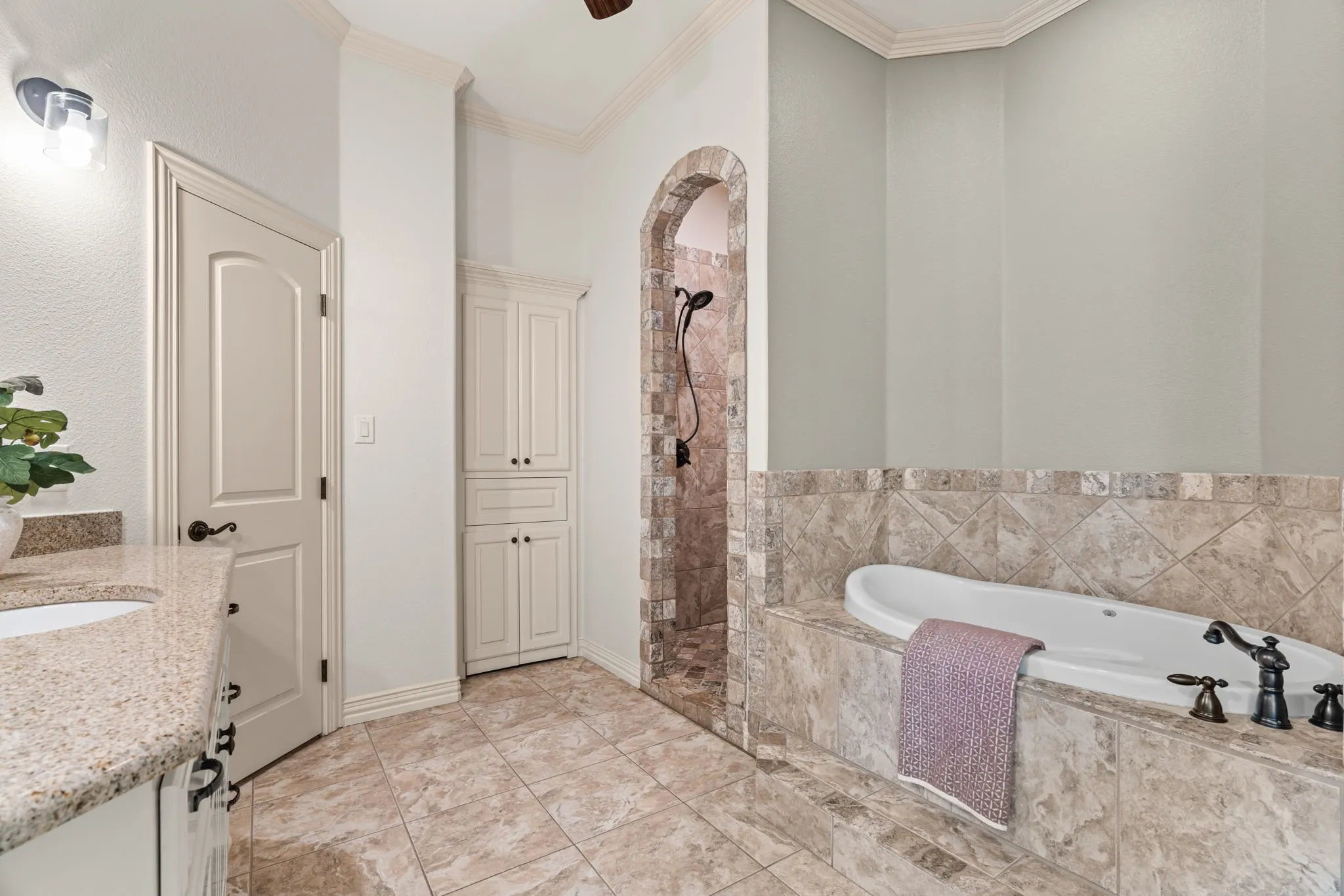 En-suite bathroom with tiled flooring, built-in soaking tub with dark bronze fixtures, archway leading to a tiled shower, built-in cabinetry, and a vanity with a light-colored countertop and 2nd closet