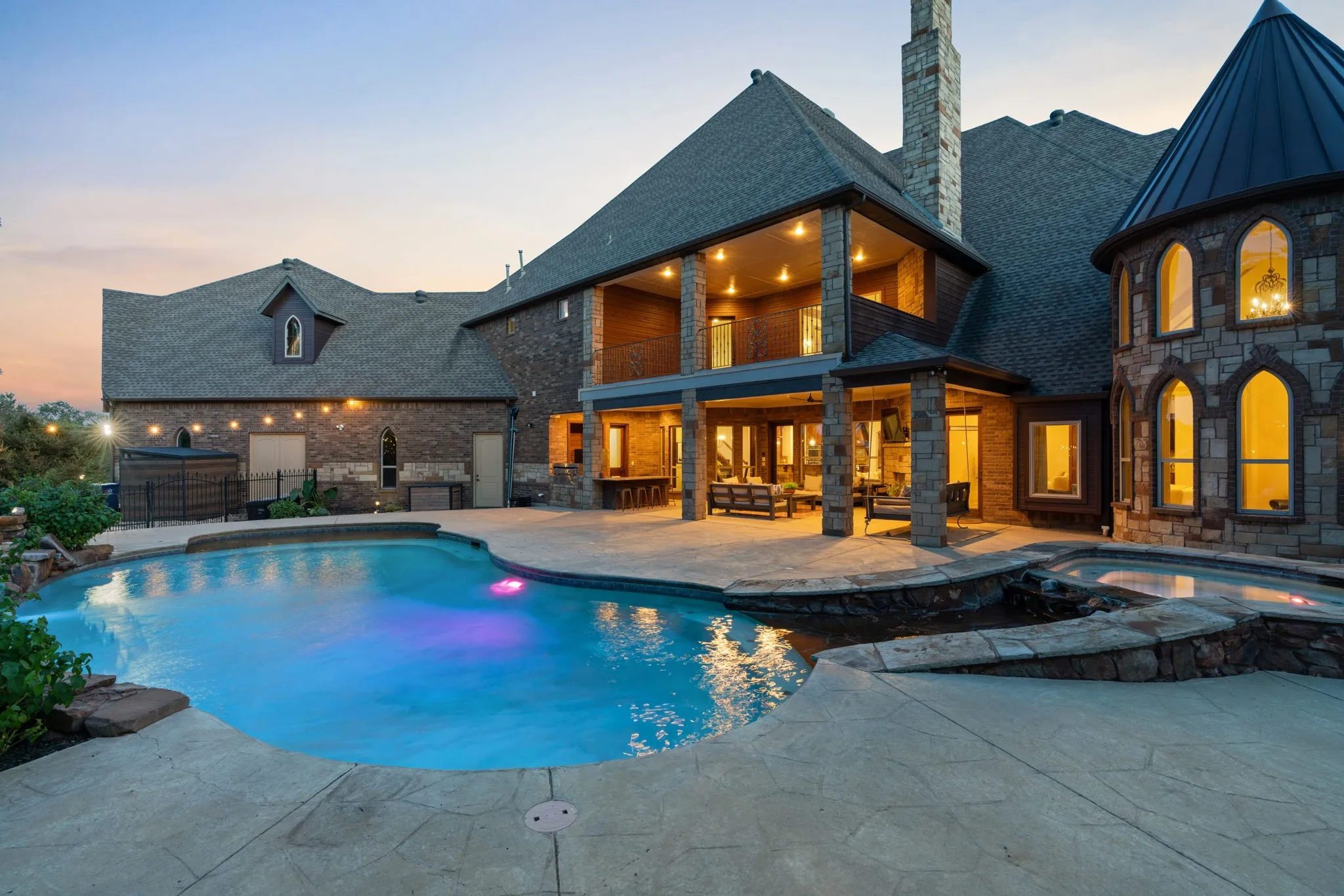 Freeform swimming pool with integrated spa and stone surround, grotto and waterslide, expansive stamped concrete patio, and covered outdoor living areas with stone columns