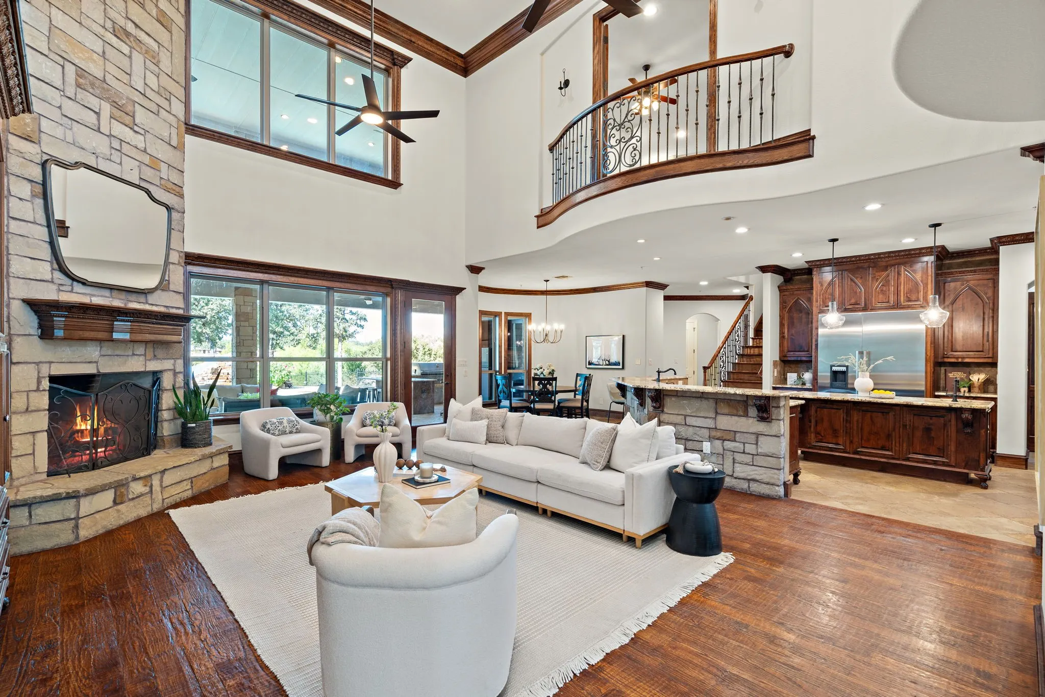 Two-story living area with a stone fireplace, wood-finish flooring, and expansive windows