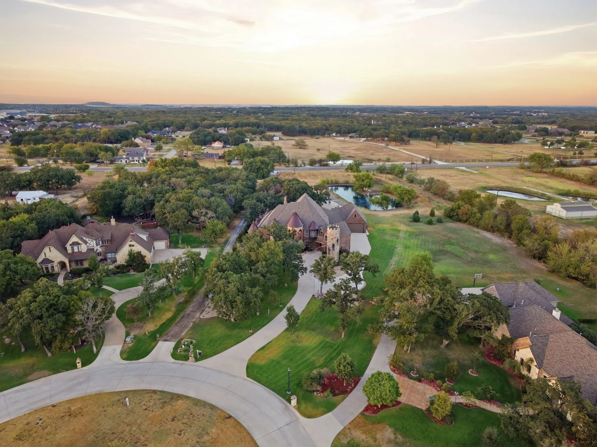 Expansive property featuring a private pond, mature trees, manicured lawns, and concrete driveways