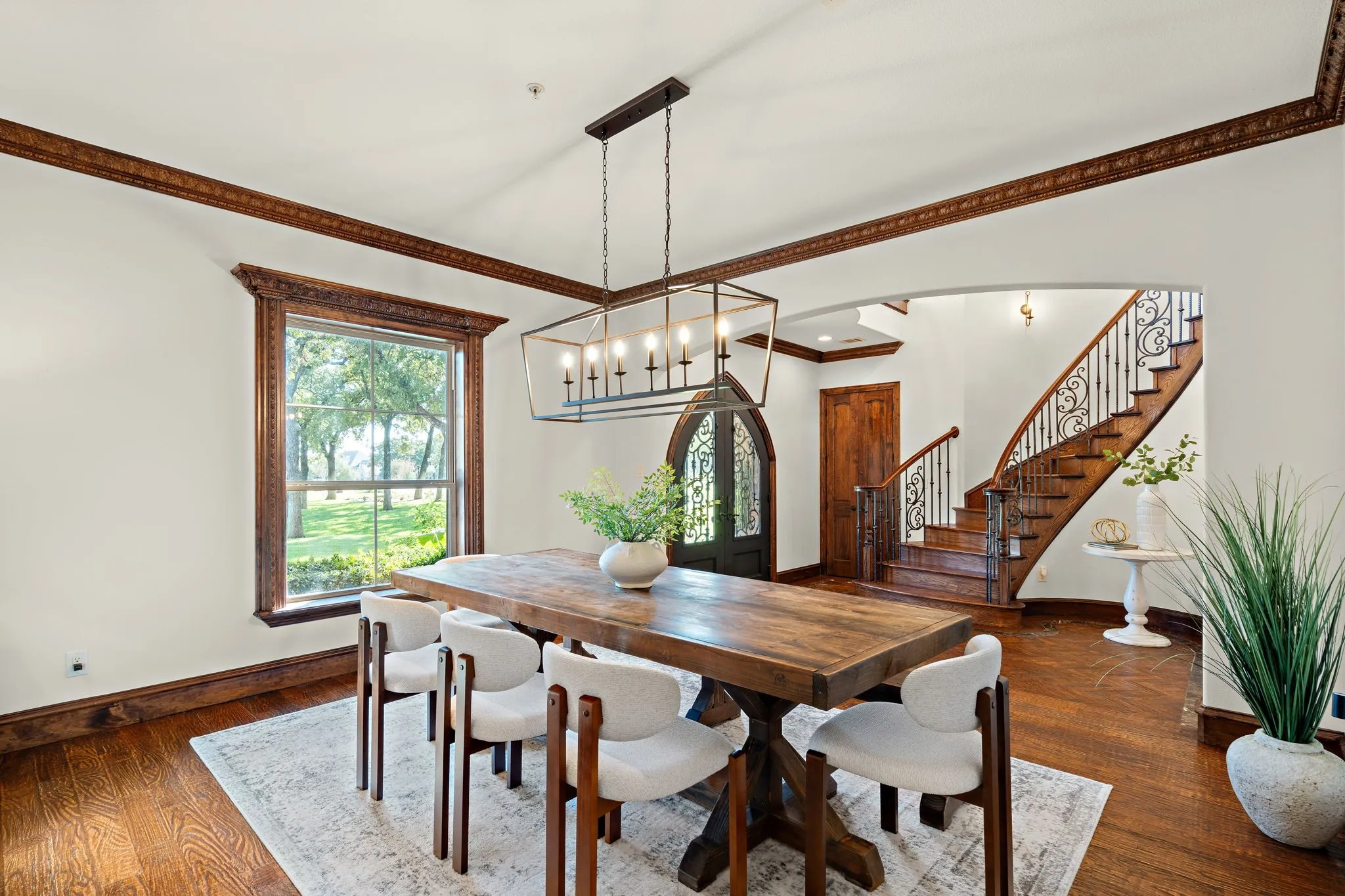 Hardwood flooring throughout, a grand staircase with wrought iron balusters, detailed wood trim, an arched entryway, and a large window