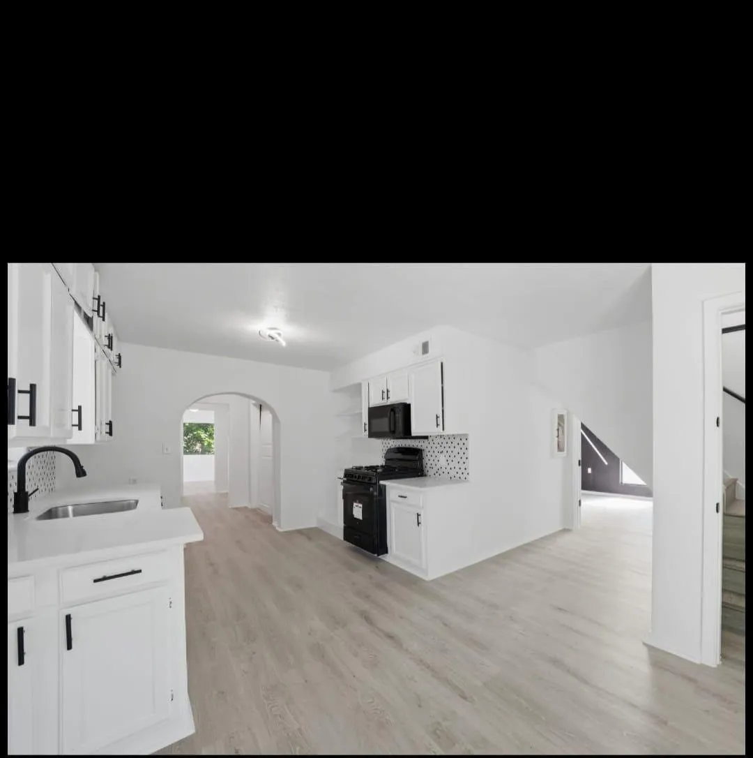 White cabinetry with matte black hardware, integrated sink with matte black faucet, light wood-finish flooring, and arched doorways
