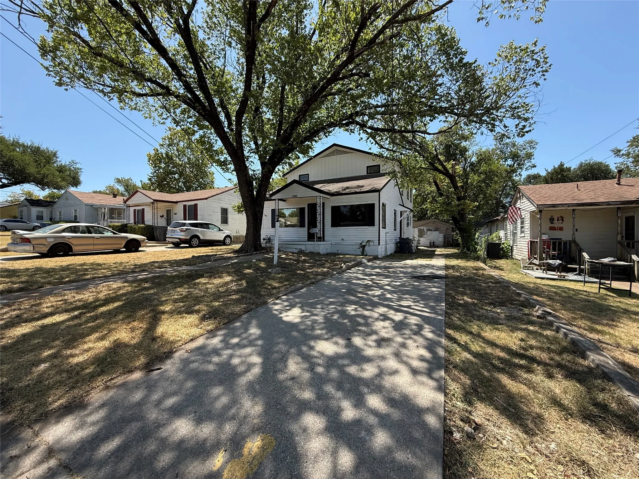 White exterior with black trim, covered porch entry, and mature trees providing natural shade