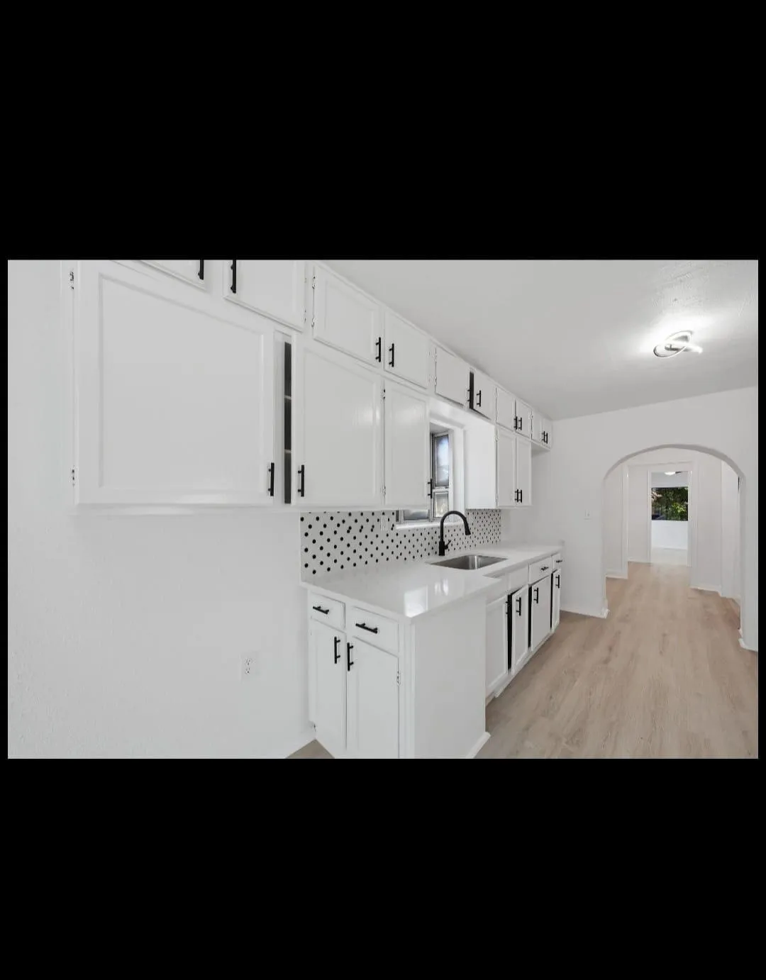 Galley kitchen featuring crisp white cabinetry with hardware accents, a polished white subway tile backsplash, stainless steel sink with modern faucet, and wood-finish flooring throughout