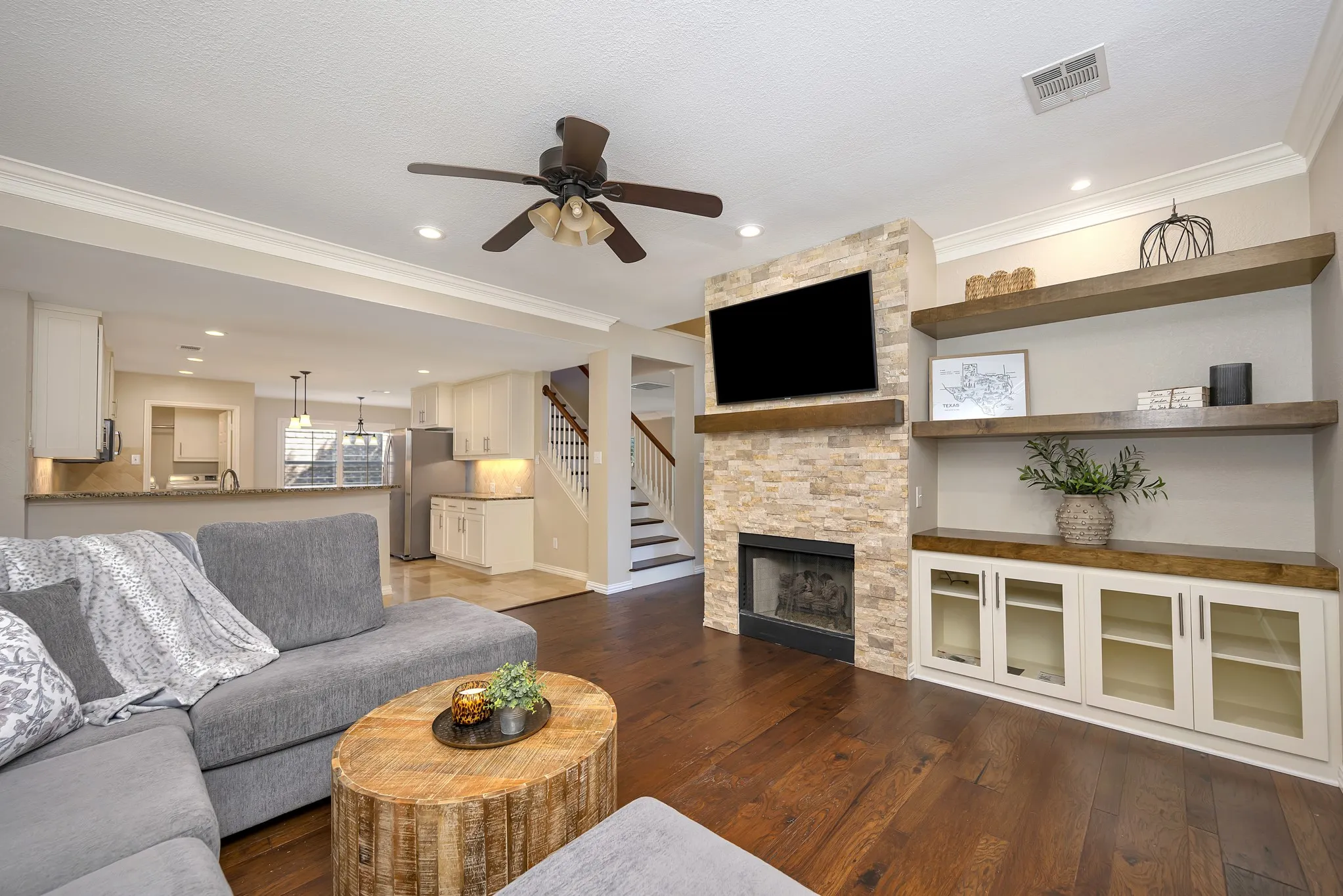 Hardwood flooring, crown molding, a stone-clad fireplace, built-in shelving, and recessed lighting