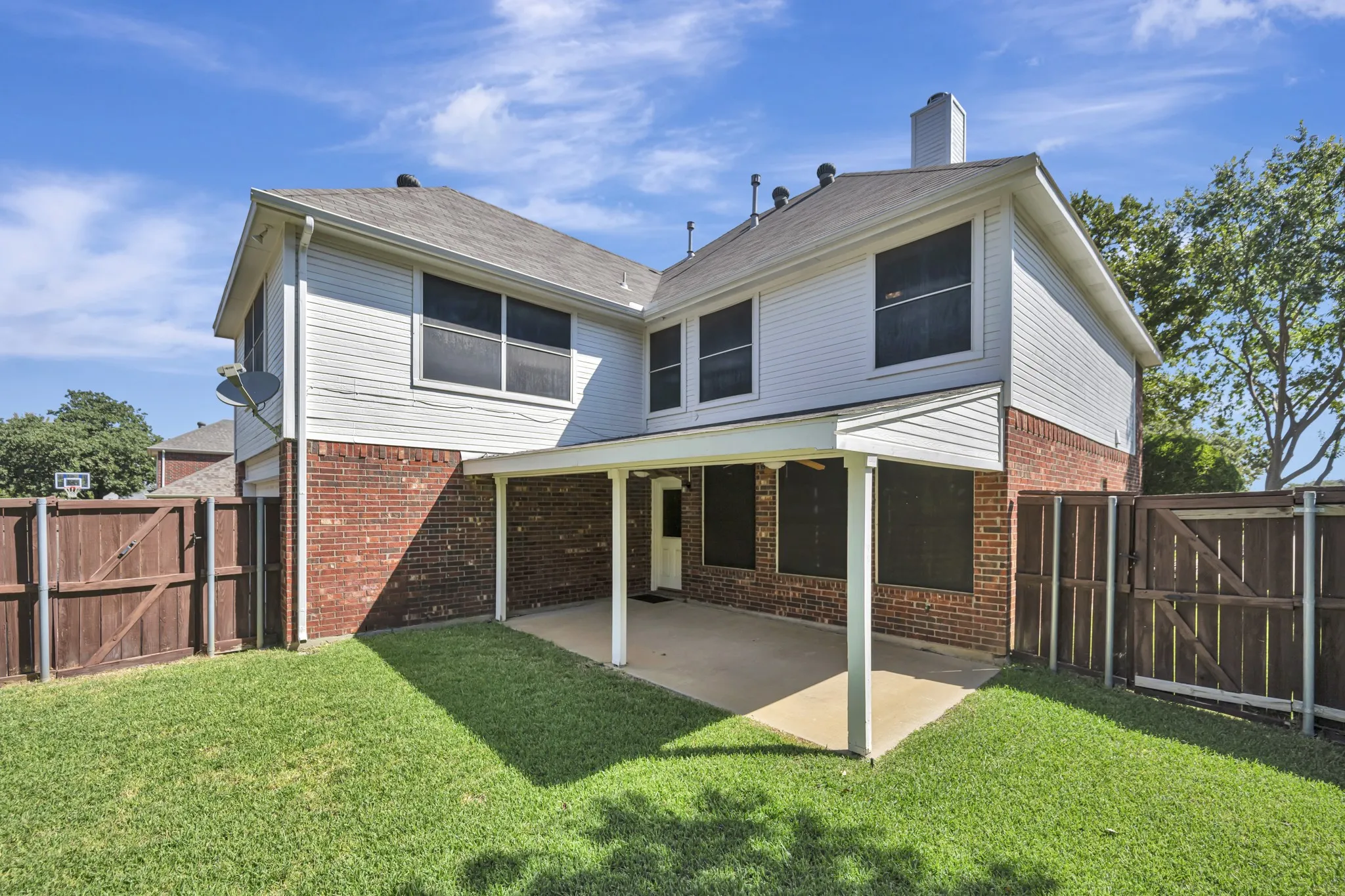 Expansive backyard featuring a covered patio, manicured lawn, brick and siding exterior, and privacy fencing