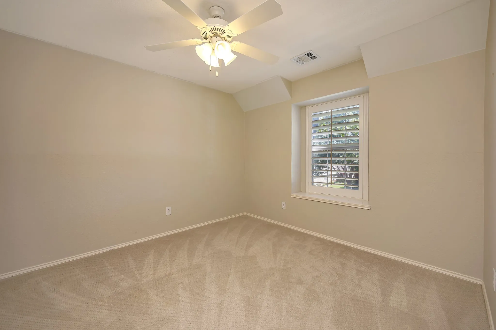 Neutral tone wall paint, carpet flooring, window with plantation shutters, ceiling fan with integrated lighting