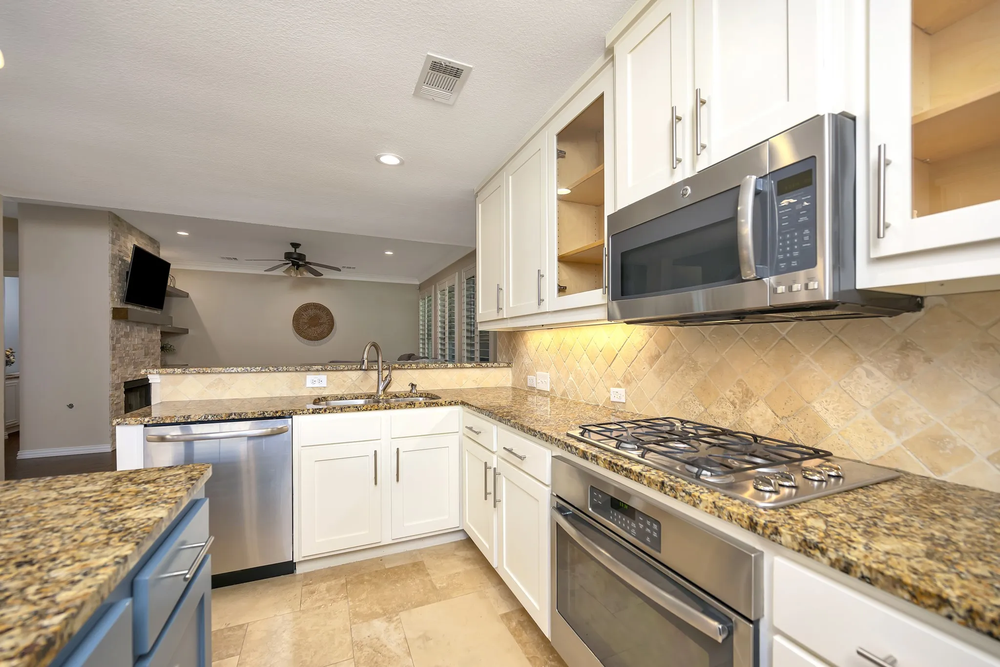 White cabinetry, stainless steel appliances, stone countertops, stone tile flooring, and a stone-clad half wall