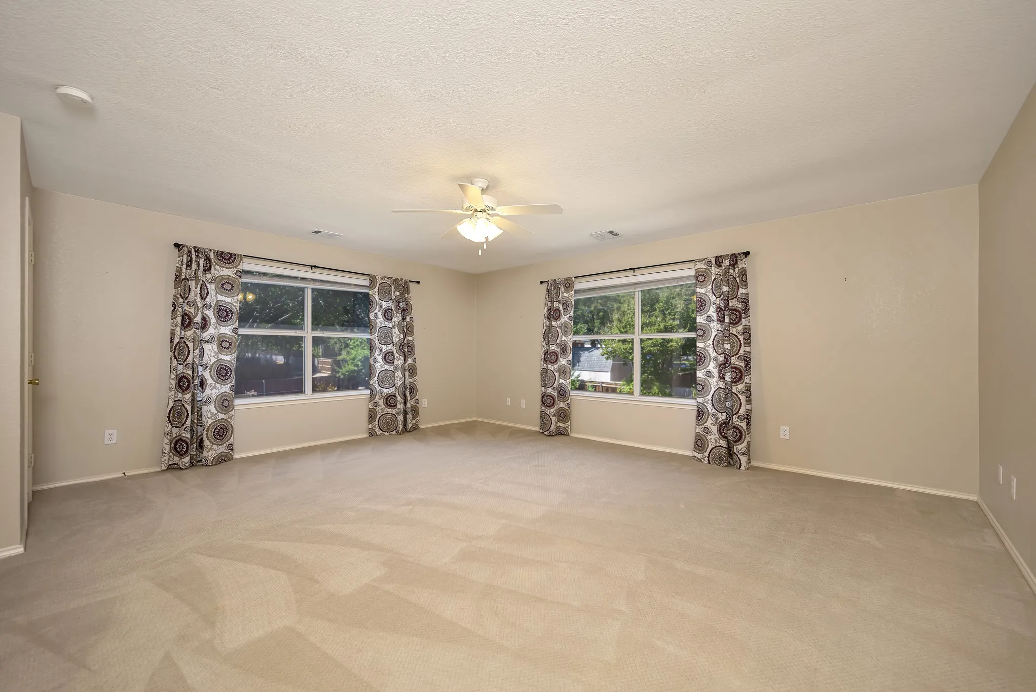 Spacious room with neutral-toned walls, plush carpeting, and two large windows