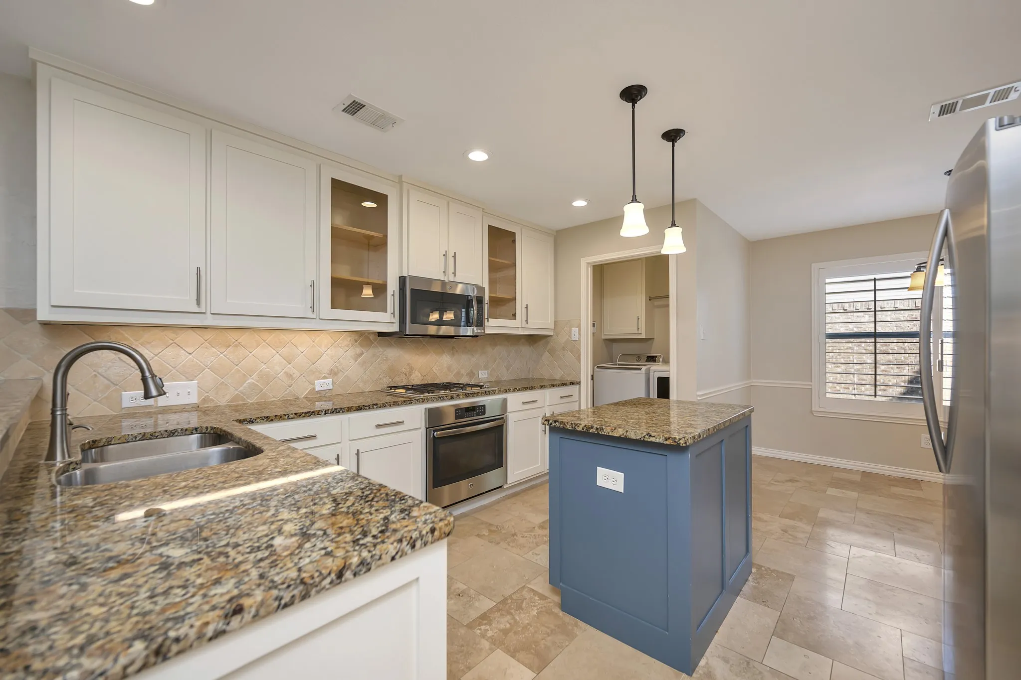 Gourmet kitchen featuring stone countertops, stainless steel appliances, a tile backsplash, white cabinetry, and a central island with pendant lighting
