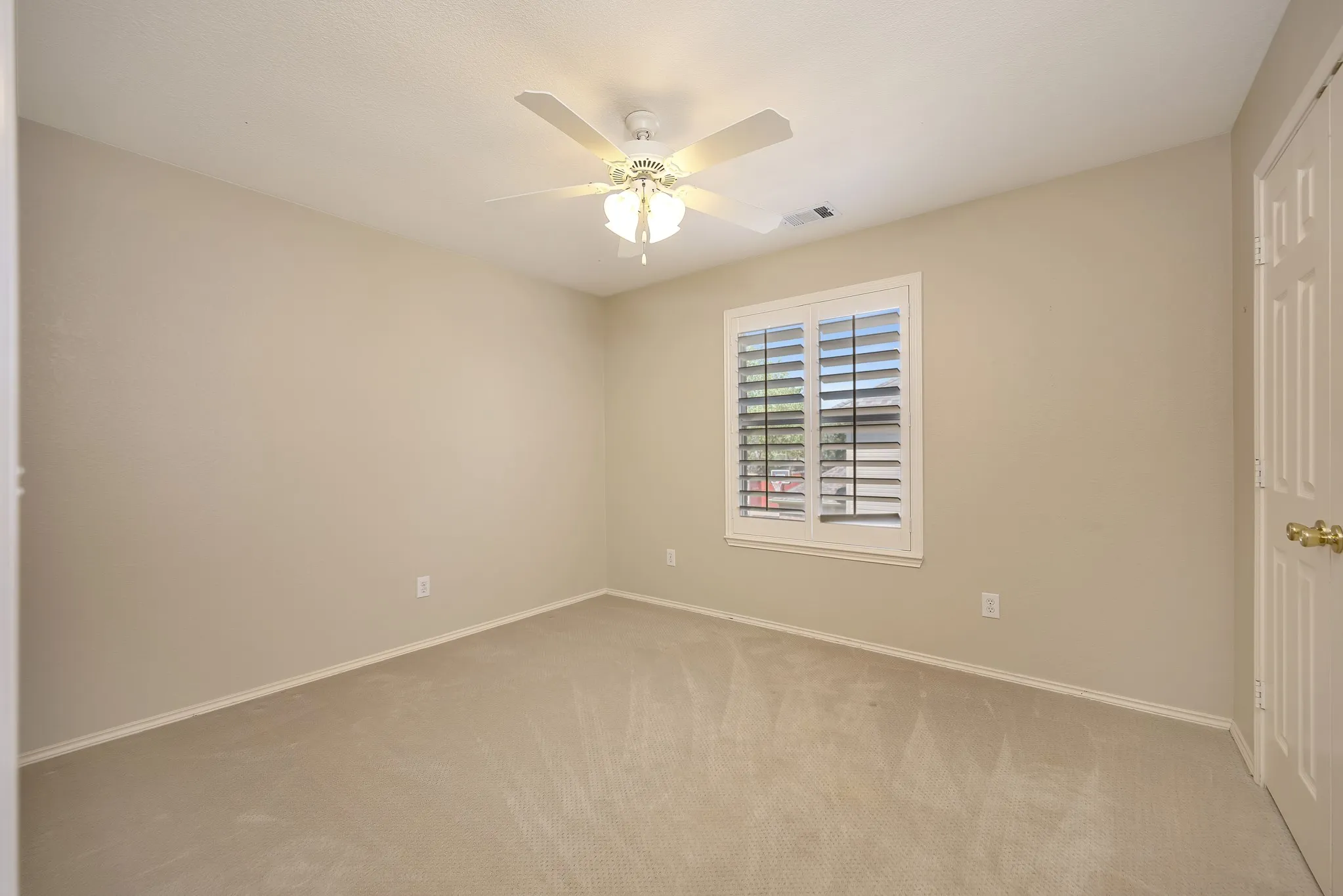 Plush carpet flooring, neutral painted walls, window with plantation shutters, and a ceiling fan with integrated lighting