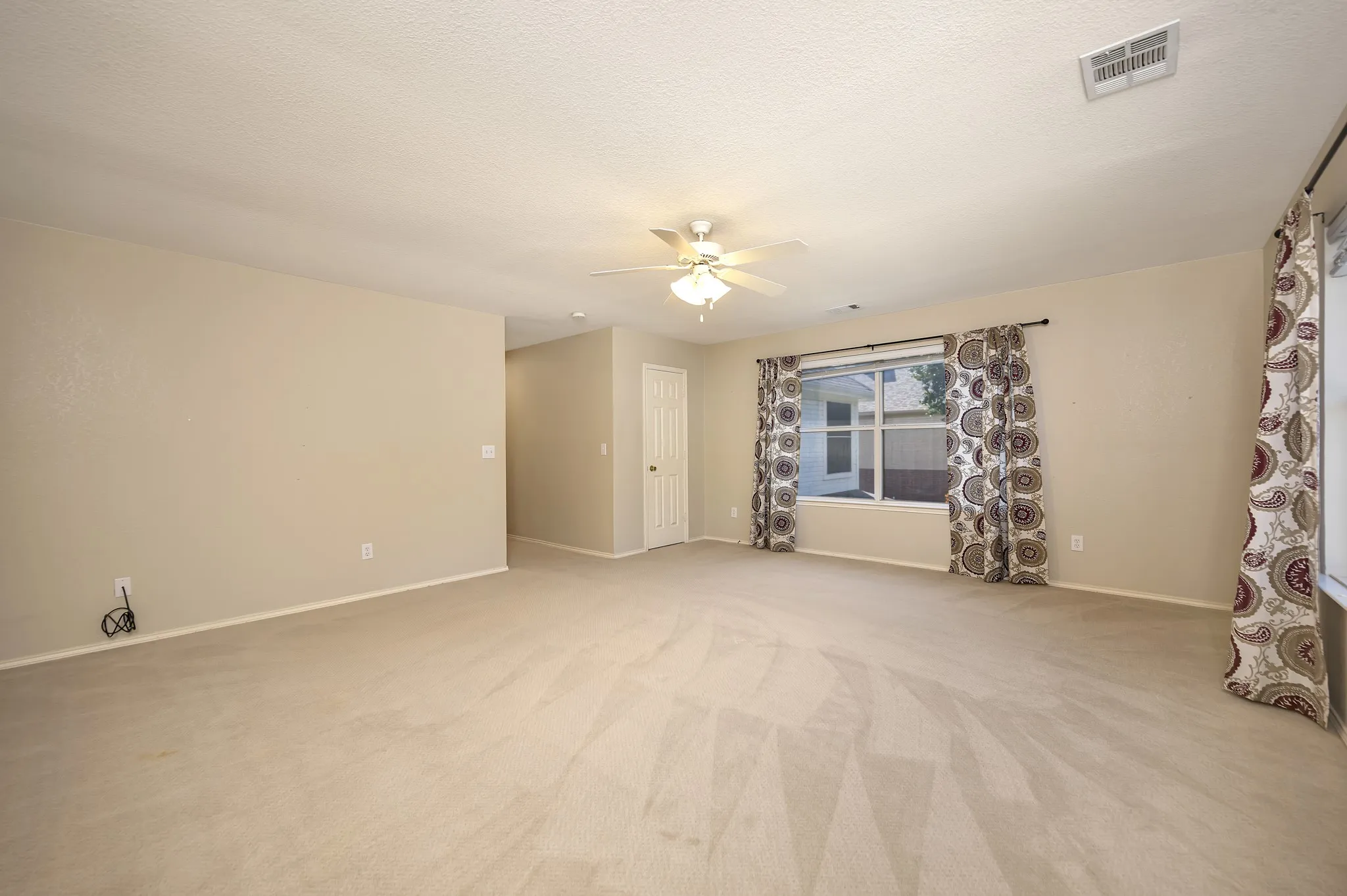 Spacious room featuring neutral carpeting, a ceiling fan with integrated lighting, and a large window with a white frame