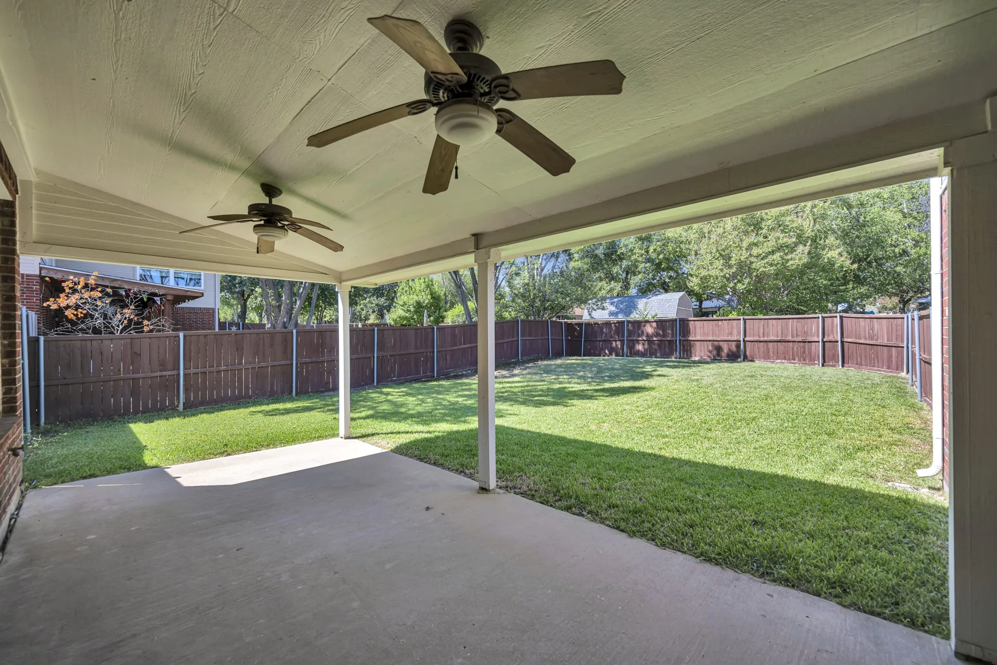 Covered patio with dual ceiling fans, concrete flooring, and direct access to a fenced yard with a manicured lawn
