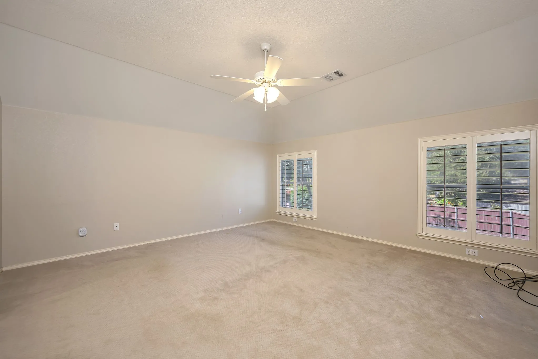 Vaulted ceiling with a ceiling fan, two windows featuring plantation shutters, and neutral carpeting
