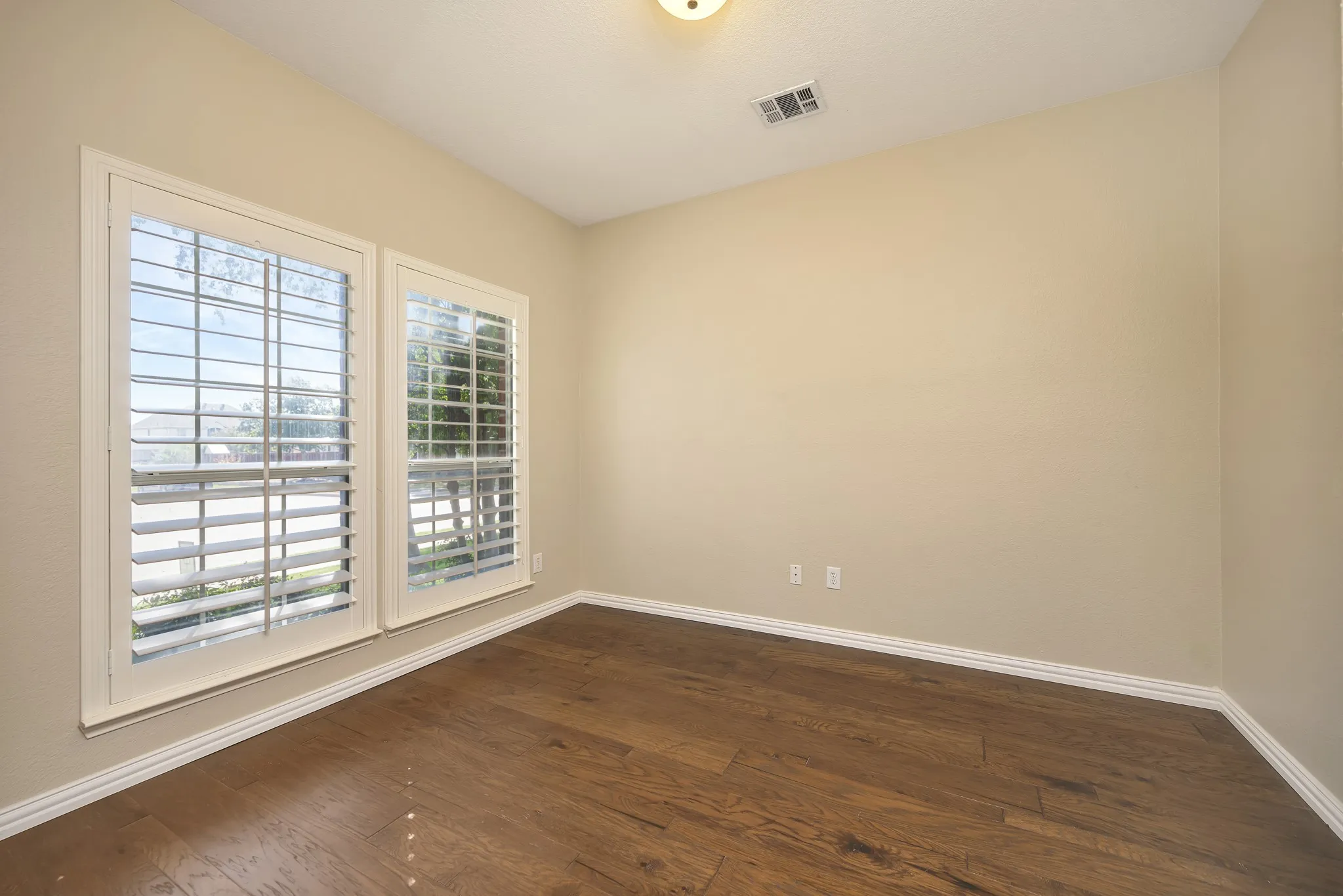 Wood-finish flooring, plantation shutters, neutral wall tones, white trim, and a flush mount ceiling light