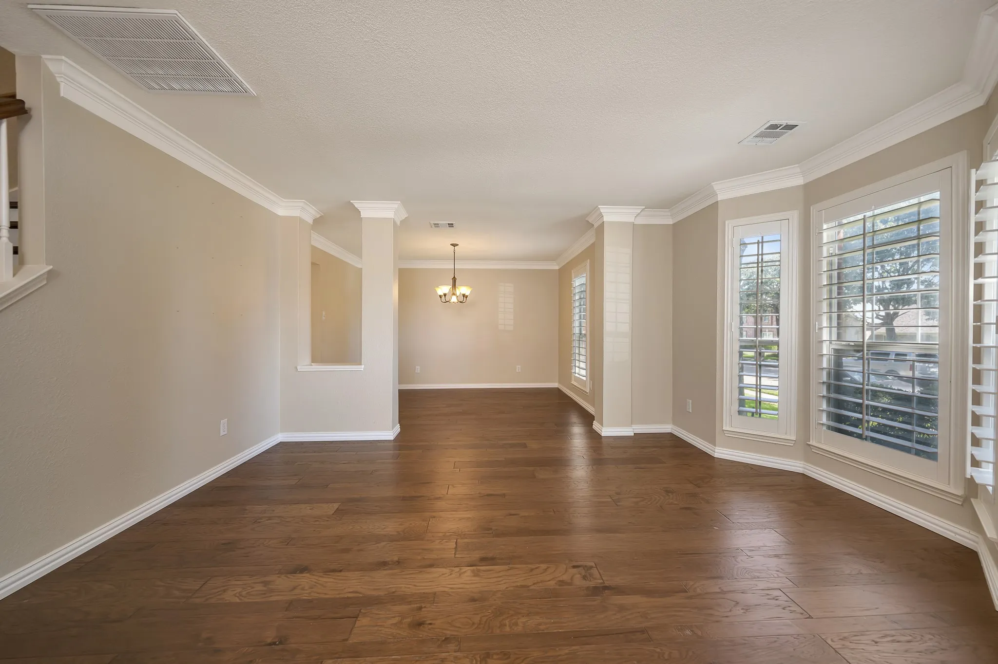 Wood-finish flooring, crown molding, plantation shutters, recessed ceiling lighting, and a chandelier in the background