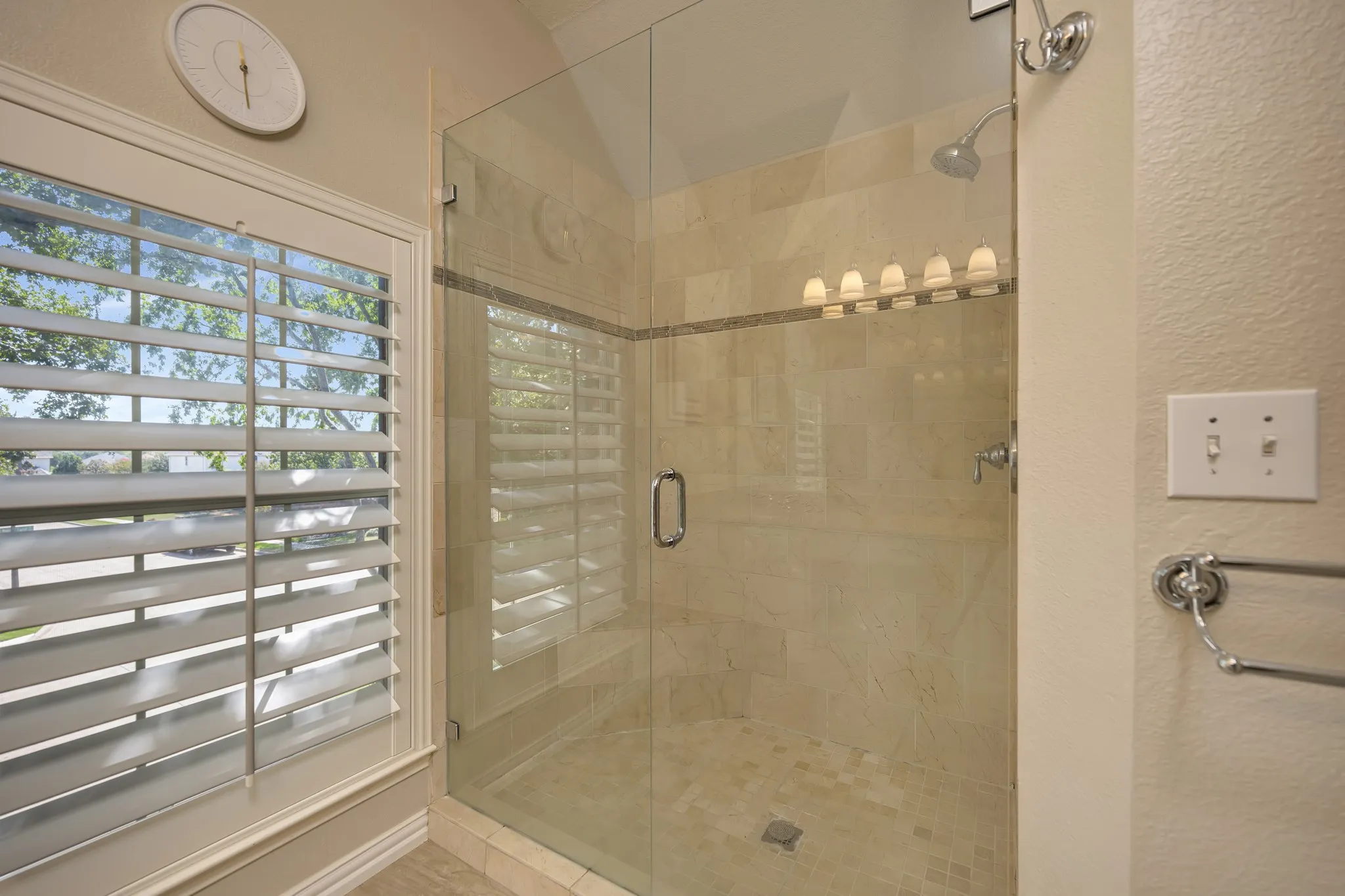 Glass-enclosed shower with tile surround and floor, chrome fixtures, and a multi-bulb vanity light