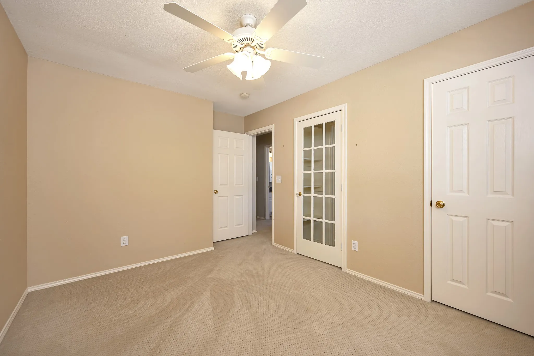 Neutral-toned carpeting, ceiling fan with integrated lighting, French panel door, and paneled interior doors