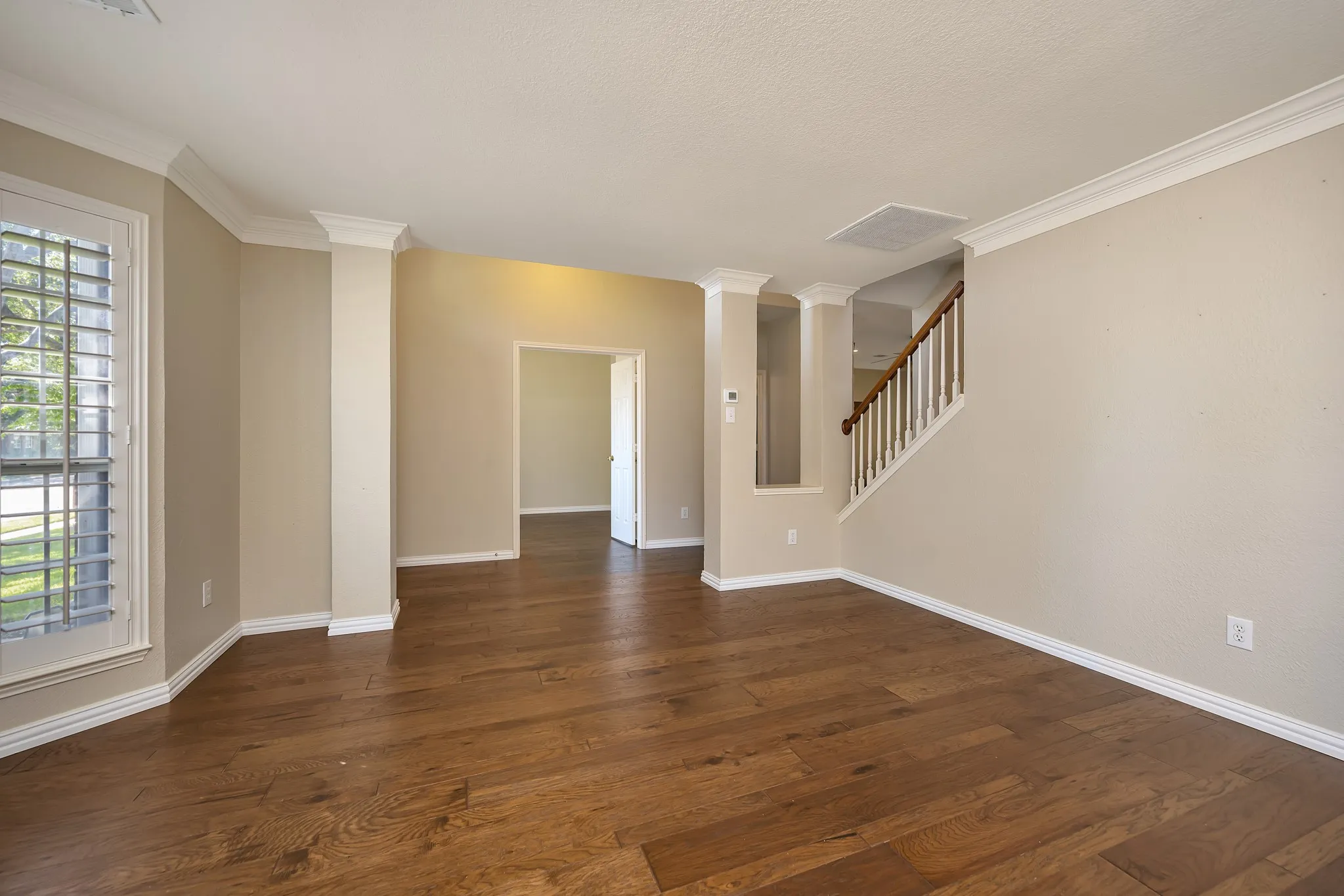 Expansive room featuring wood-finish flooring, white crown molding, and plantation shutters