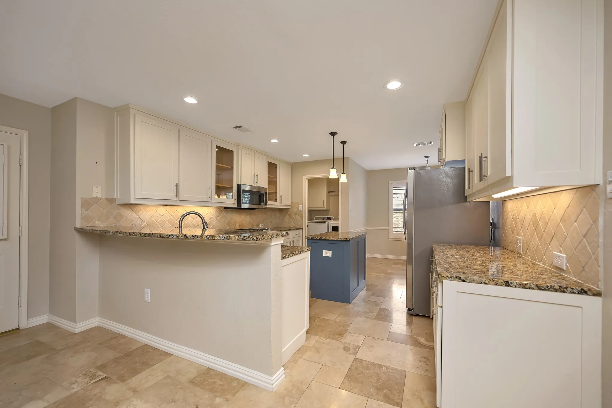 Kitchen featuring white cabinetry, stone tile flooring, stainless steel appliances, a blue kitchen island, and recessed lighting