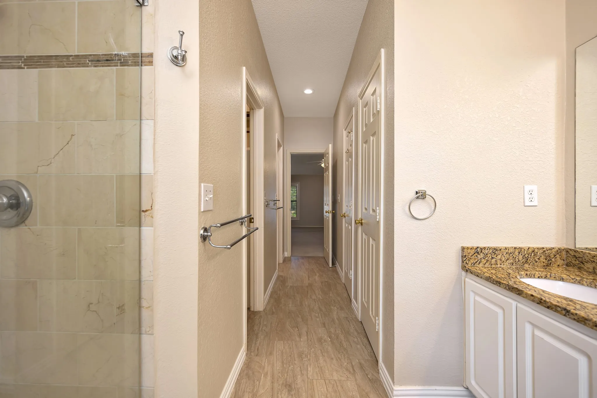 Shower with glass enclosure and tiled surround, wood-finish flooring, recessed lighting, and a vanity with a stone countertop