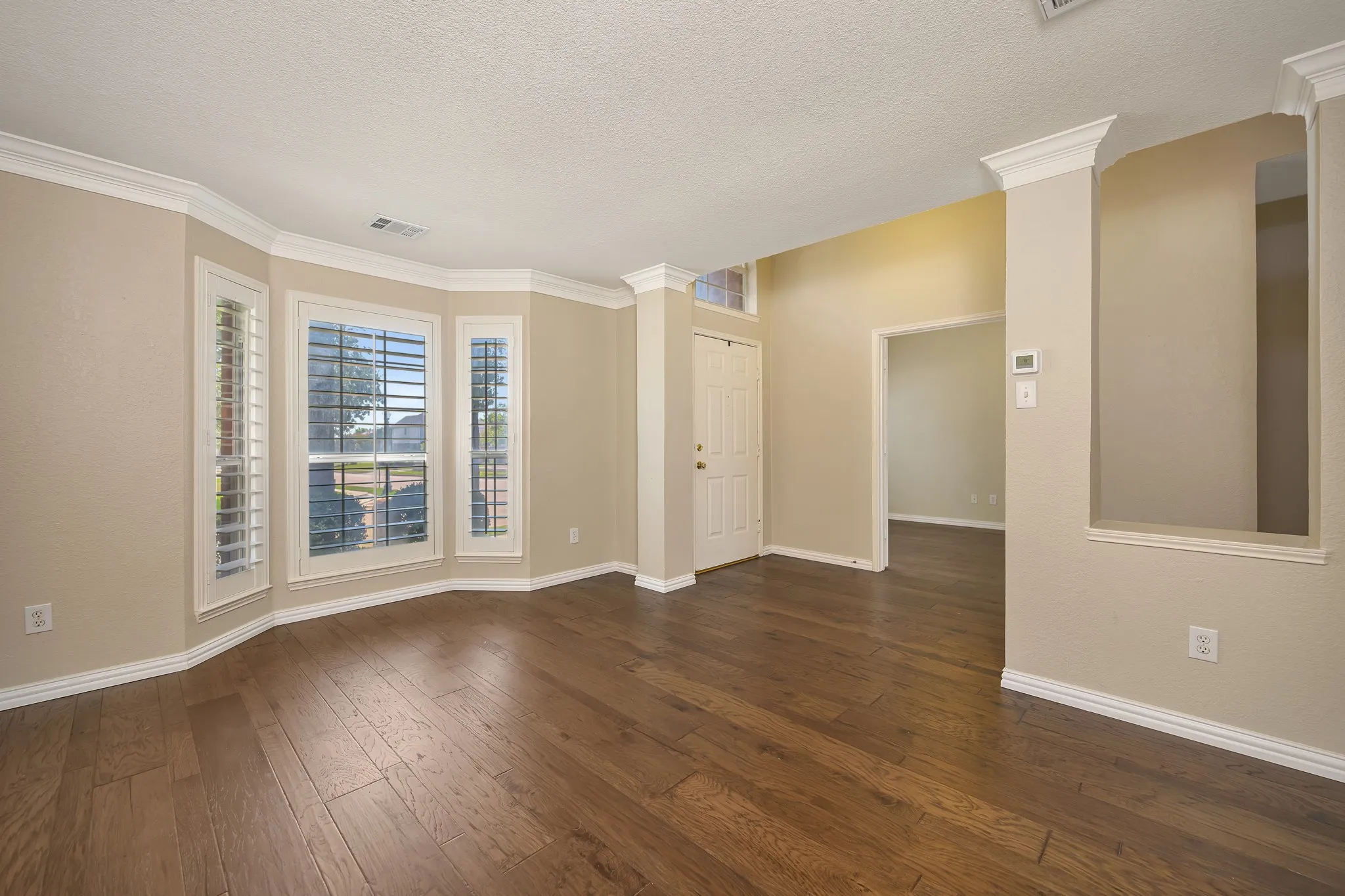 Bay windows with plantation shutters, crown molding, wood-finish flooring, and recessed wall niche