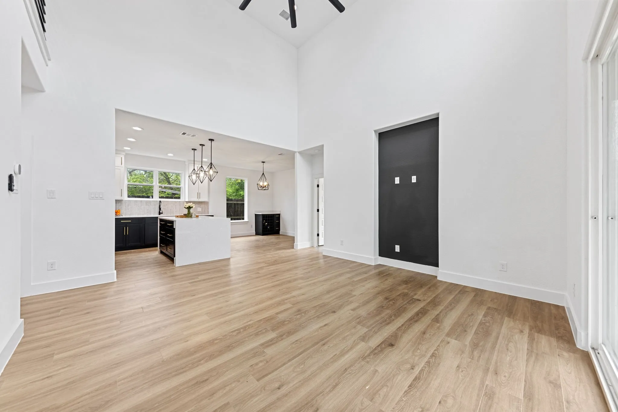 Vaulted ceilings, wood-finish flooring, a kitchen island, dark cabinetry, and geometric pendant lighting