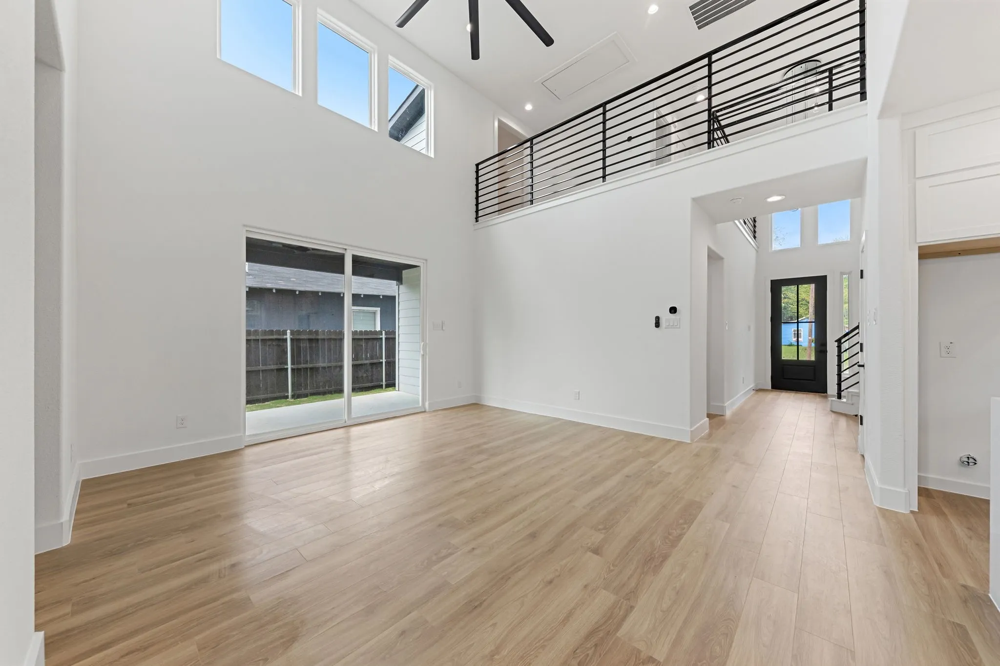 Two-story living area with wood-finish flooring, high ceilings, large sliding glass doors, and a second-story balcony with horizontal metal railings