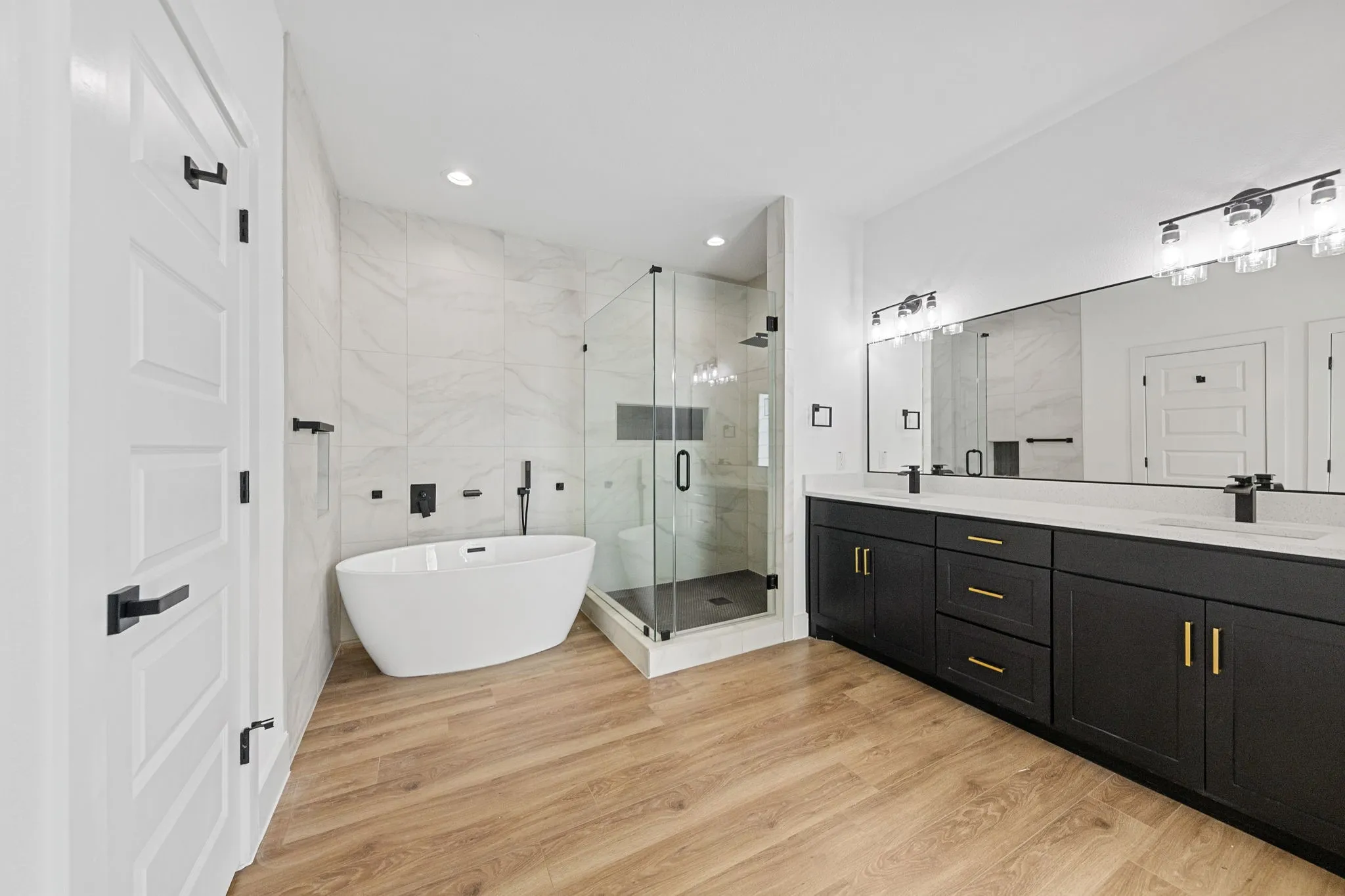 Wood-finish flooring, a freestanding soaking tub with wall-mounted fixtures, and a glass-enclosed shower with tile surround