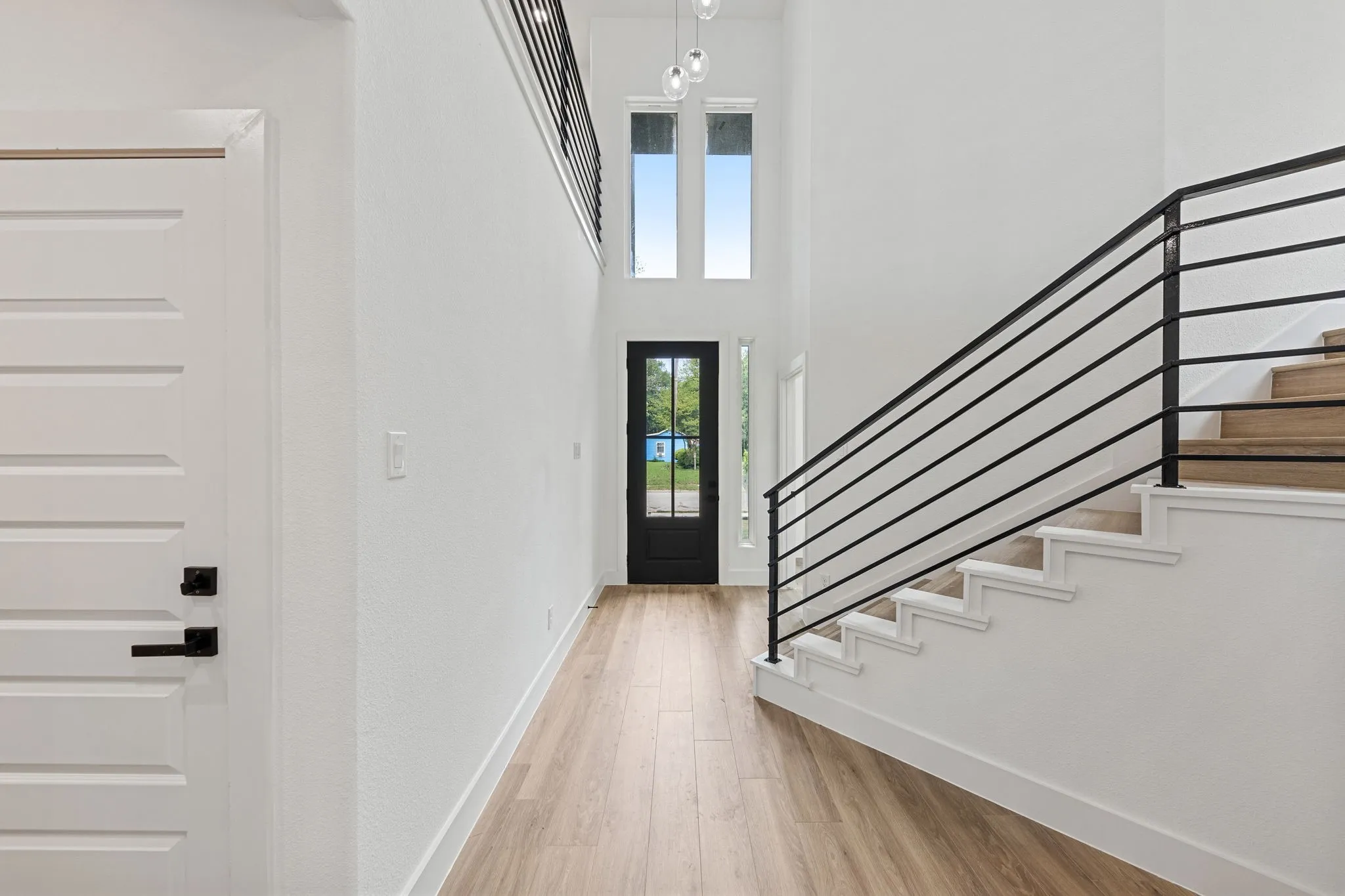 Two-story entry featuring wood-finish flooring, a contemporary chandelier, a black framed glass door, and a staircase with an open riser design and horizontal metal railing