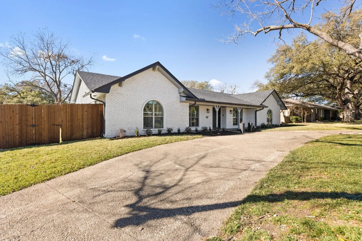 White brick ranch home featuring a welcoming front elevation with arched entry portico, black architectural shutters, and manicured lawn