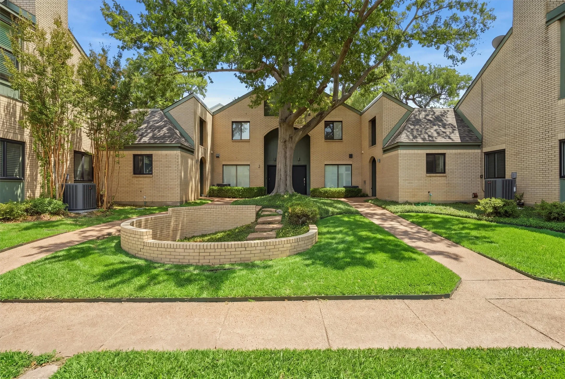 Framed by a towering mature oak and manicured green grounds, this striking brick exterior delivers immediate curb appeal and a serene entryway.