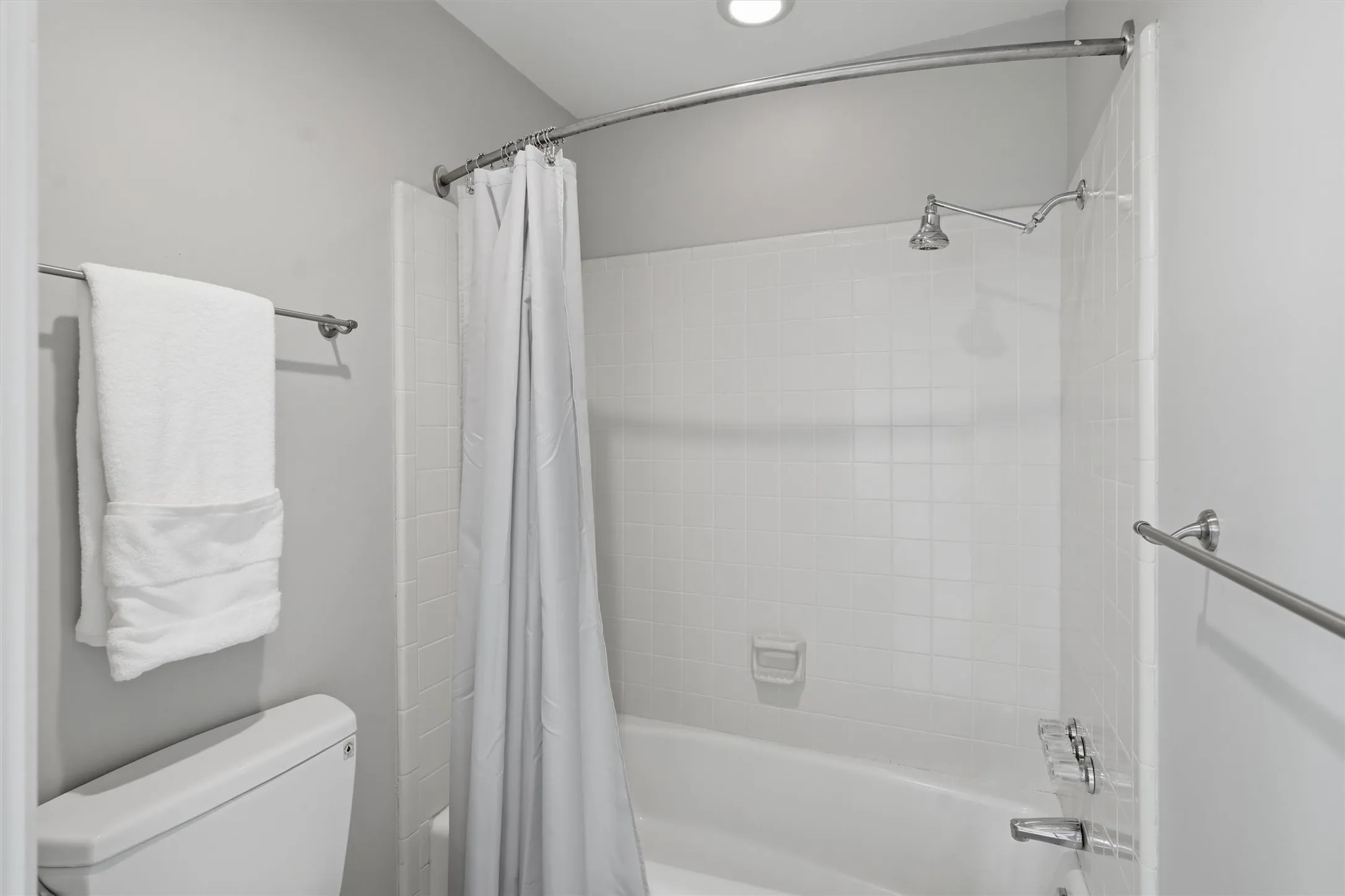 Tucked privately off the main vanity, this clean primary bath nook features classic white tile surround, a full tub-and-shower combination, and crisp neutral finishes.