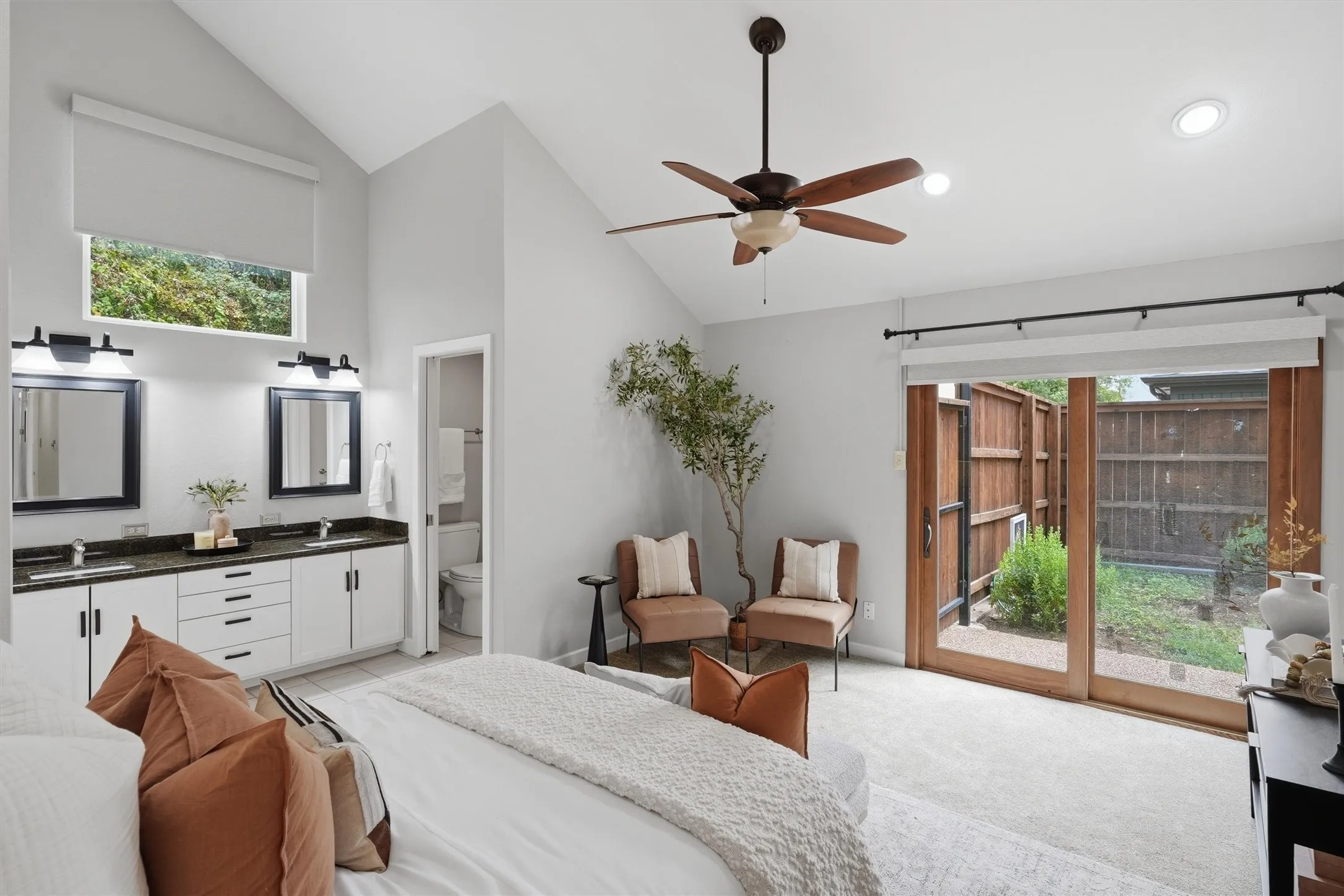 This spacious primary suite serves as a private sanctuary, featuring dramatic vaulted ceilings, an integrated double-vanity bathroom, and direct sliding door access to a secluded outdoor patio.