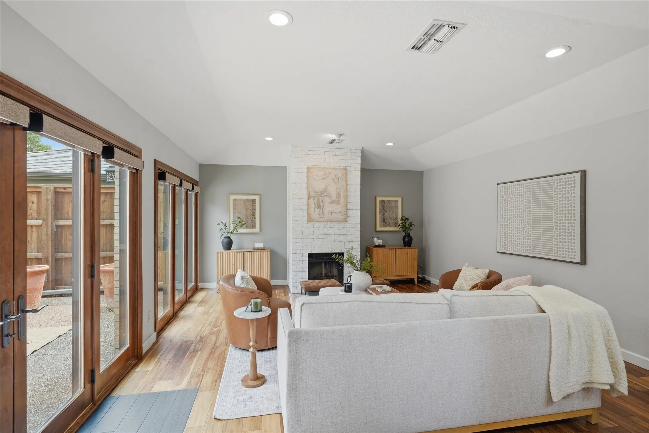 Flooded with natural light from a wall of wood-framed patio doors this wide living space showcases woodlike floors, airy, flexible layout anchored by a white bricked fireplace.