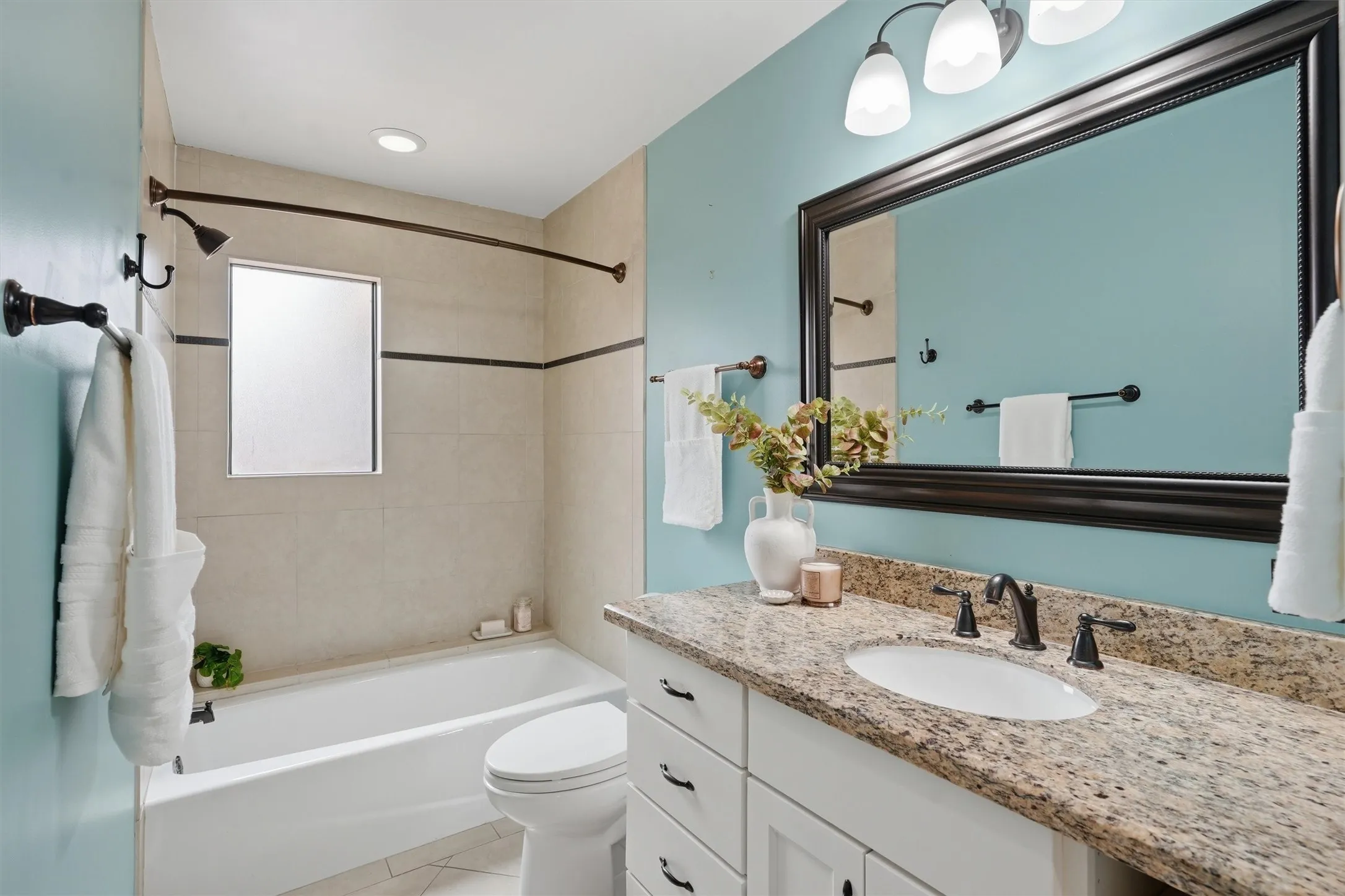 This full secondary bathroom combines style and function with granite countertops, oil-rubbed bronze fixtures, a full tub-and-shower combination, and a frosted window for private natural light.