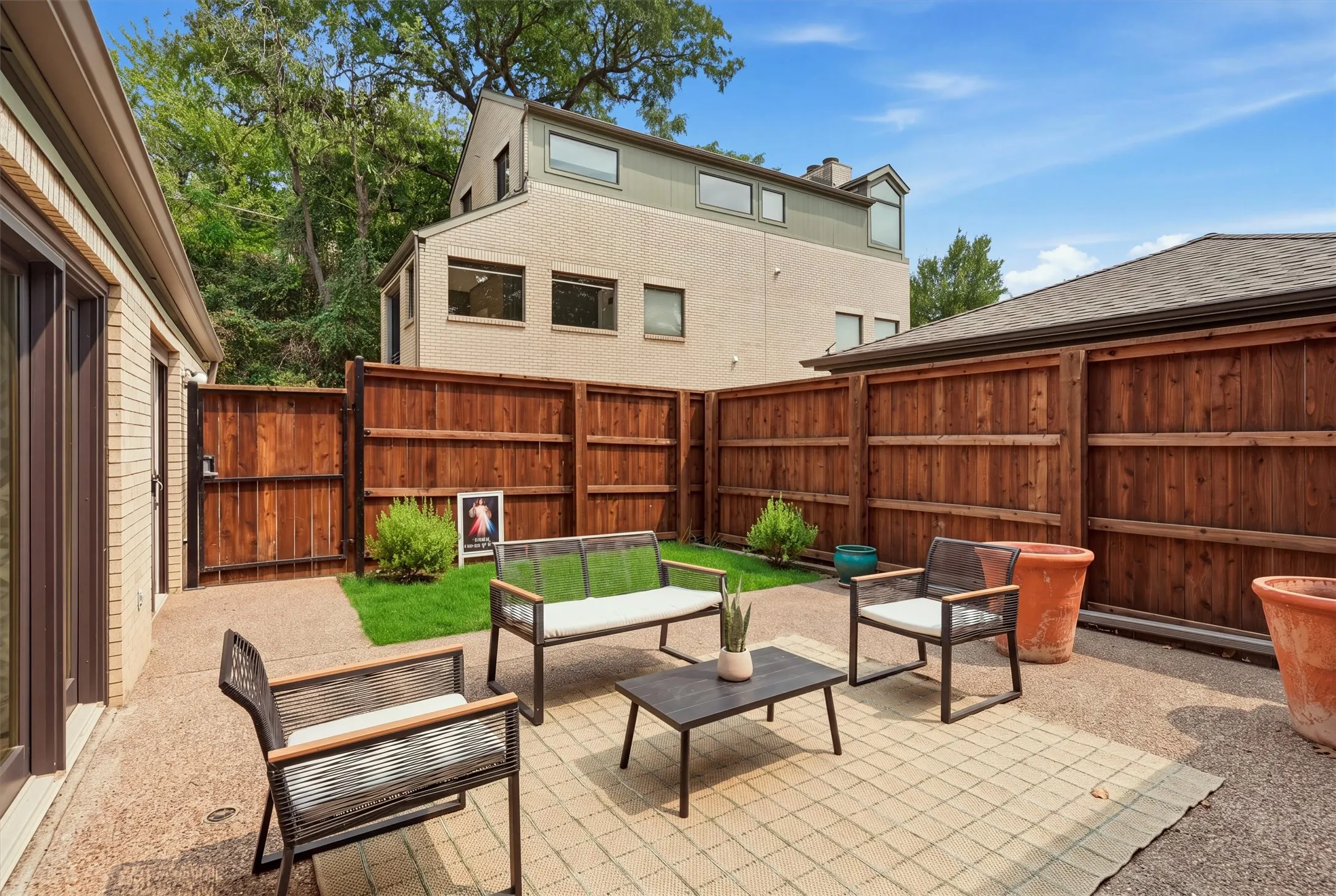Fully enclosed by a tall wooden privacy fence, this serene outdoor patio features aggregate paving, a lawn accent, and gated access to create a low-maintenance, private backyard retreat.