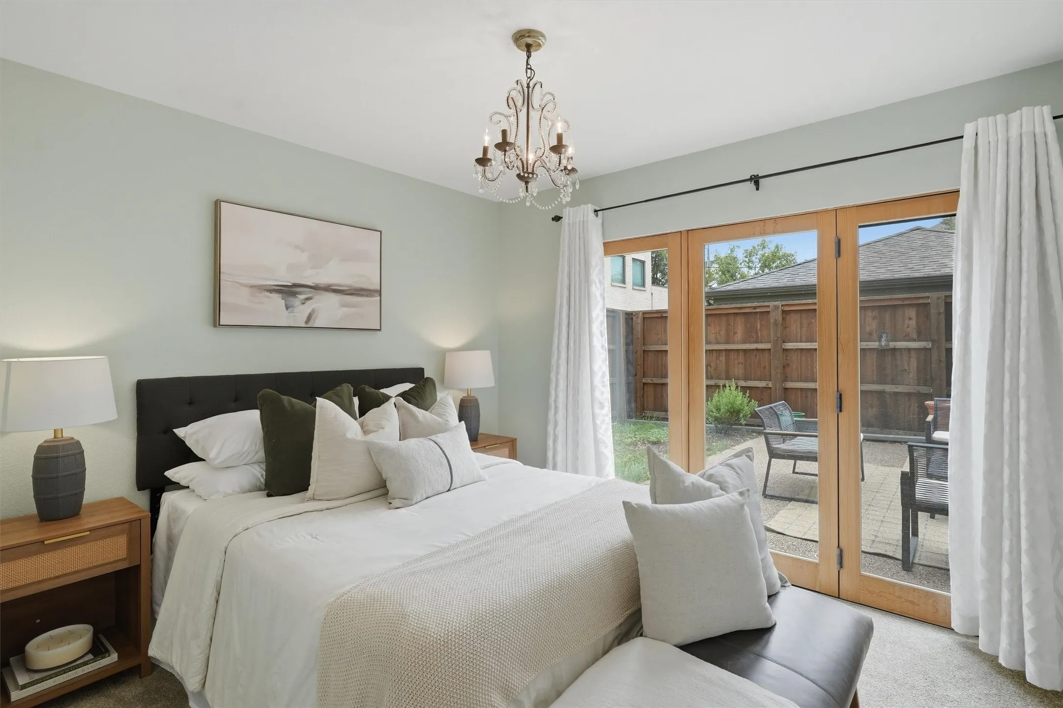 Highlighted by a charming central chandelier, this inviting secondary bedroom features soft neutral tones and private French doors that open directly to the outdoor patio.