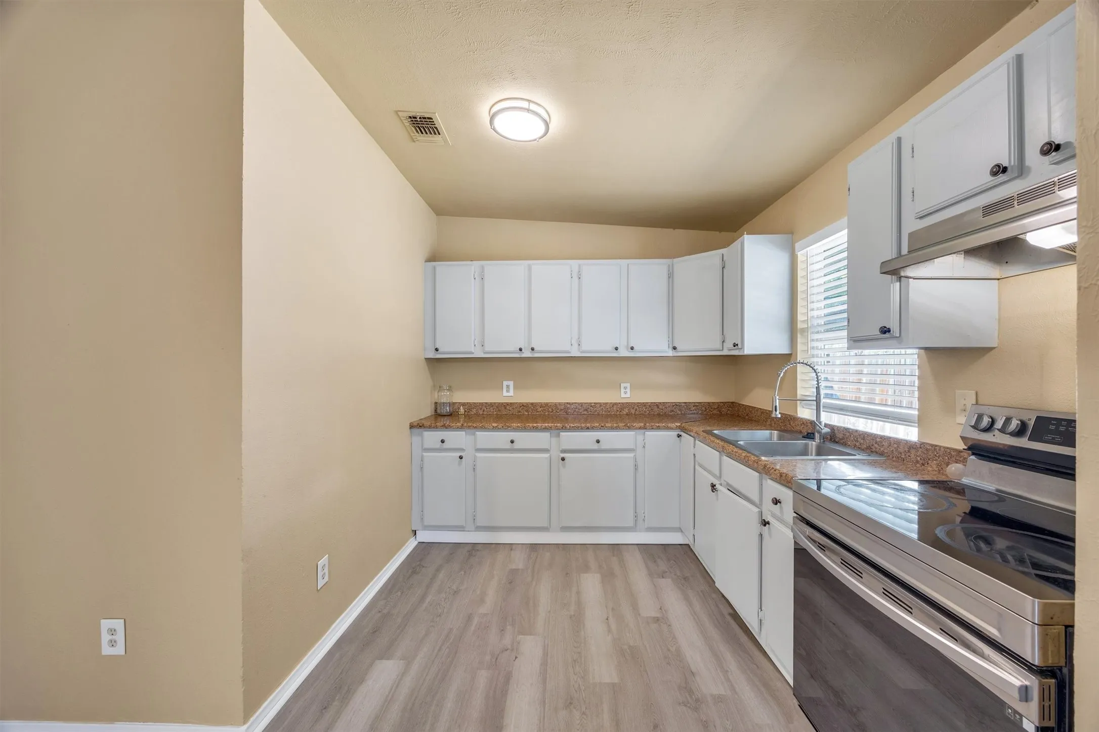 Kitchen featuring white cabinetry, wood-finish flooring, stainless steel appliances, a double basin sink, and a window with blinds