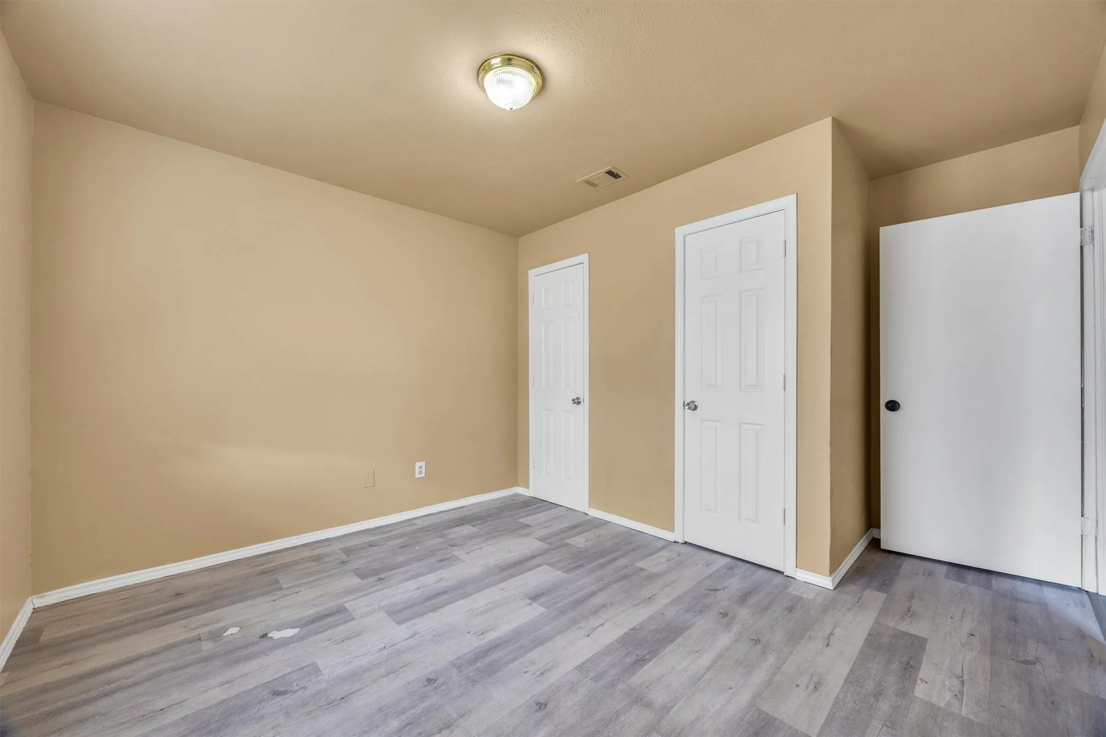 Wood-finish flooring with a neutral wall color, white trim, and multiple white panel doors