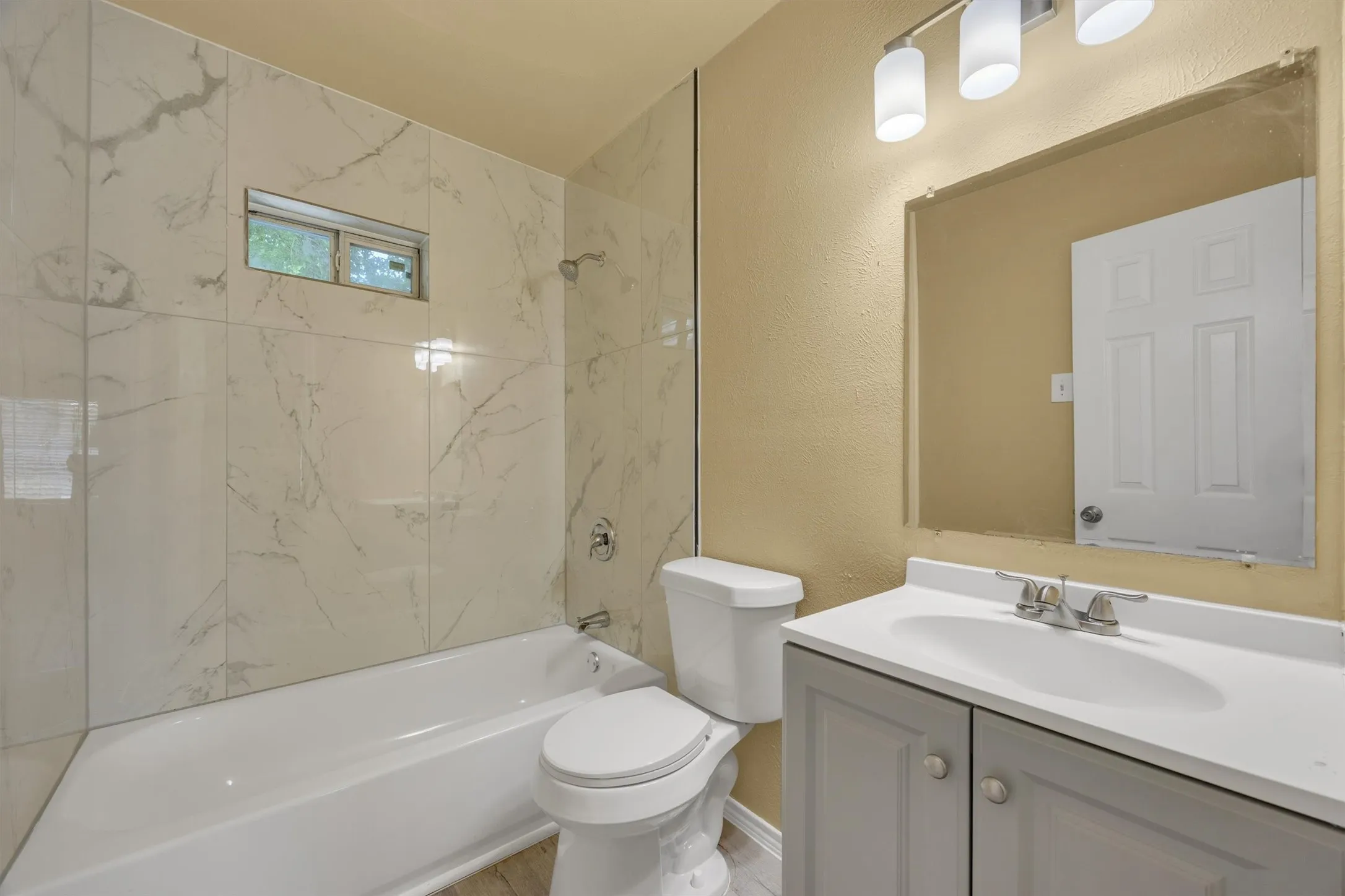 Spa-inspired bathroom featuring marble-look tile surround with seamless glass enclosure, white porcelain fixtures, and dual vanity with ample counter space